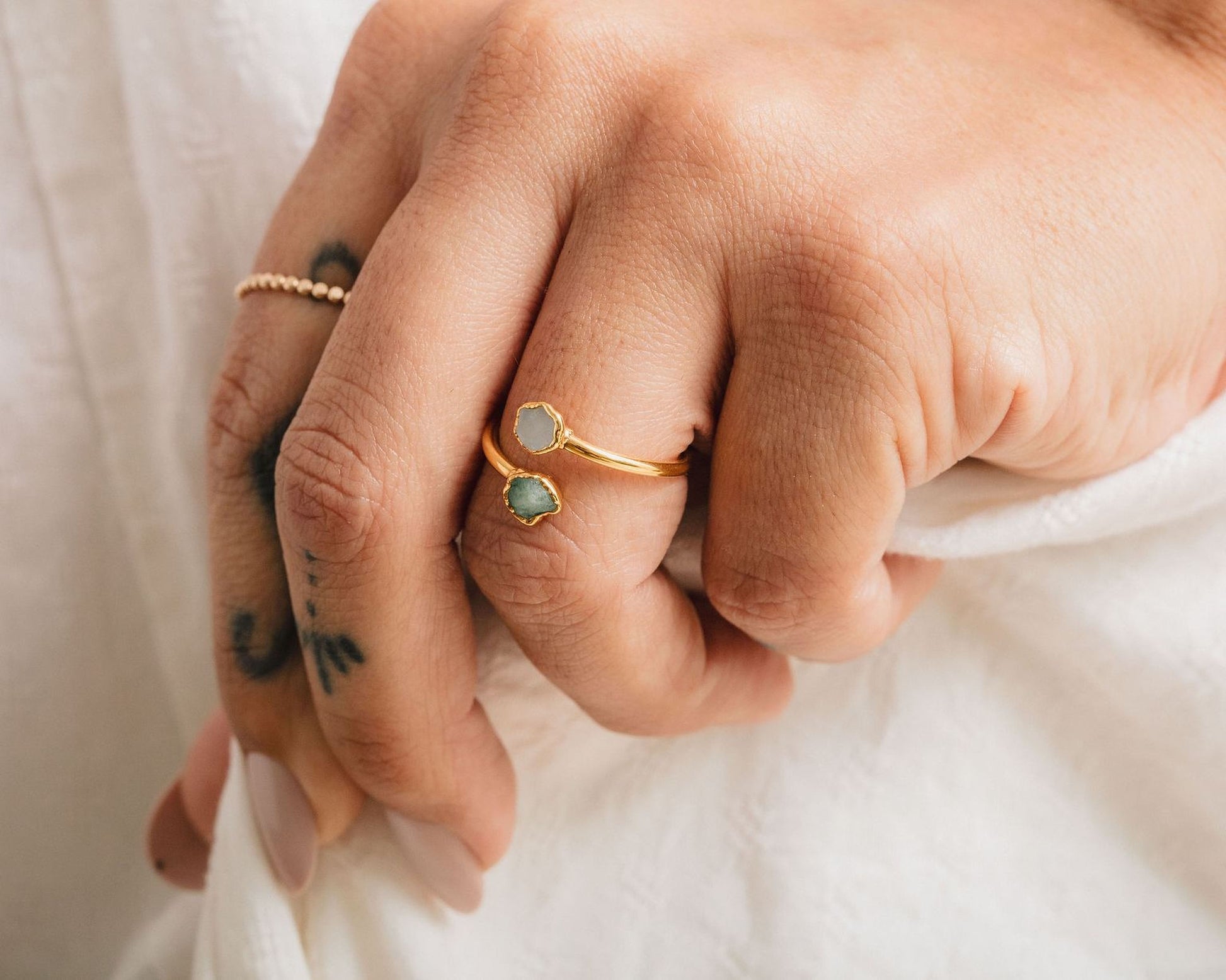 A close-up view of a person's hand wearing a gold ring with two green gemstones.