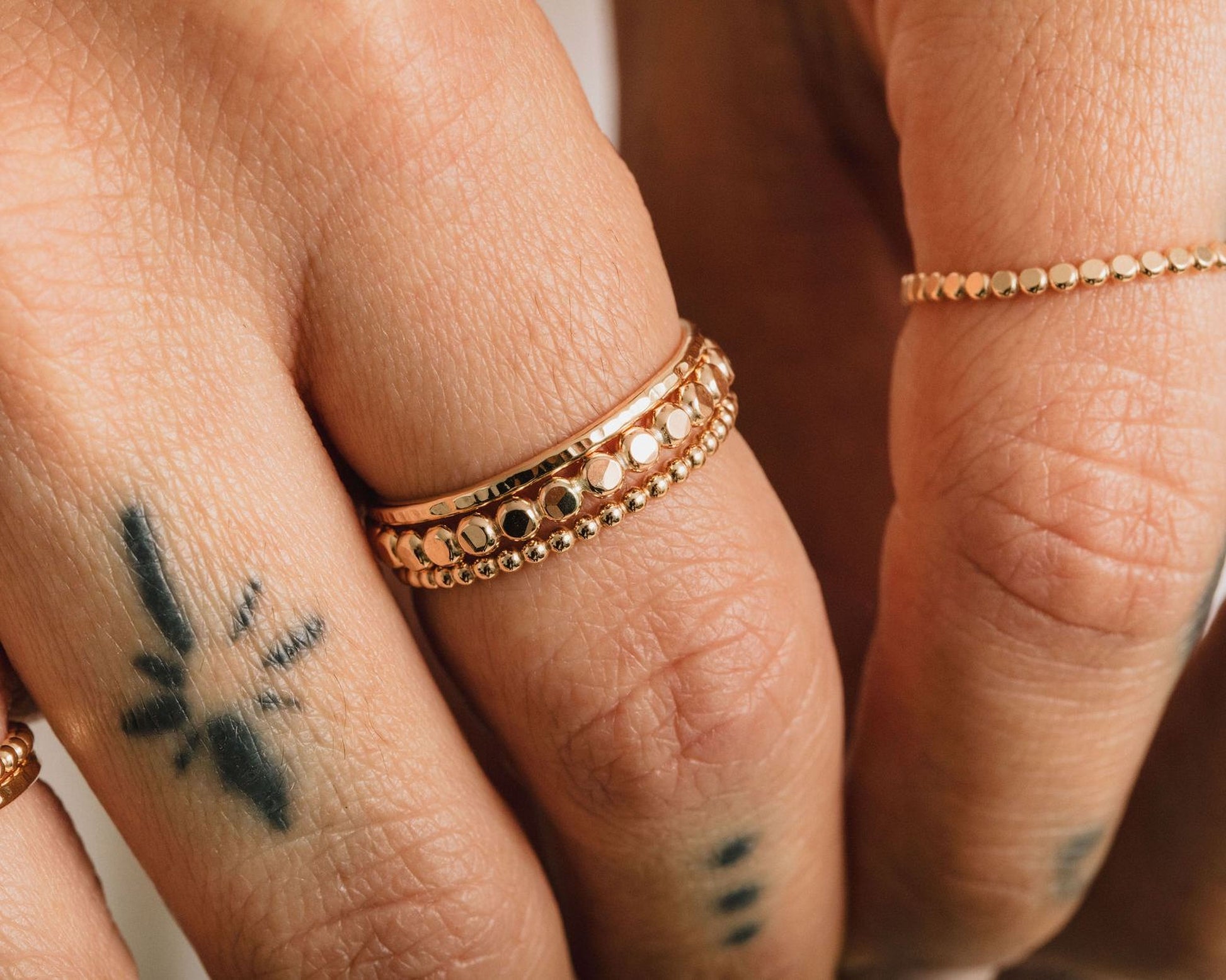 A close-up of a person's hand wearing multiple gold rings on the fingers.