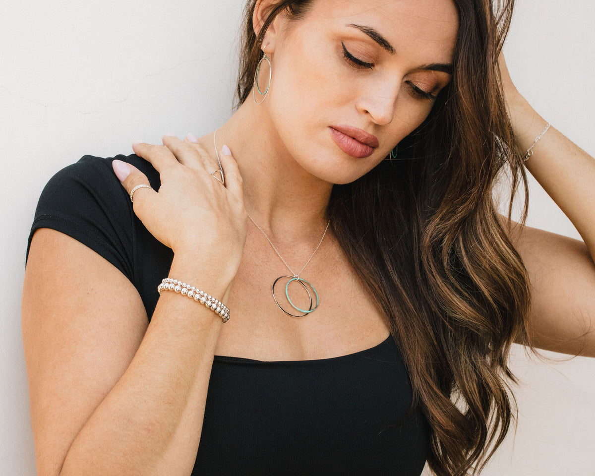 A woman with long brown hair wearing a black top and jewelry poses against a white background.