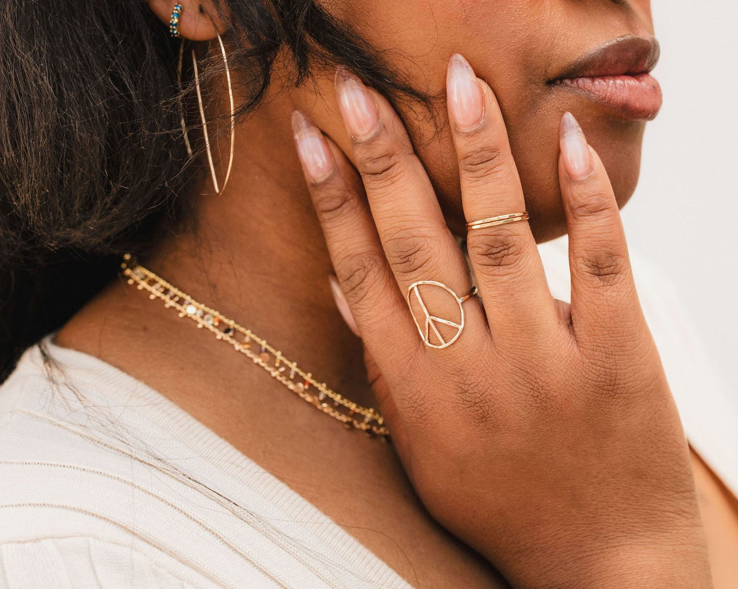 A close-up of a person's face, focusing on their hand adorned with multiple rings and jewelry pieces.