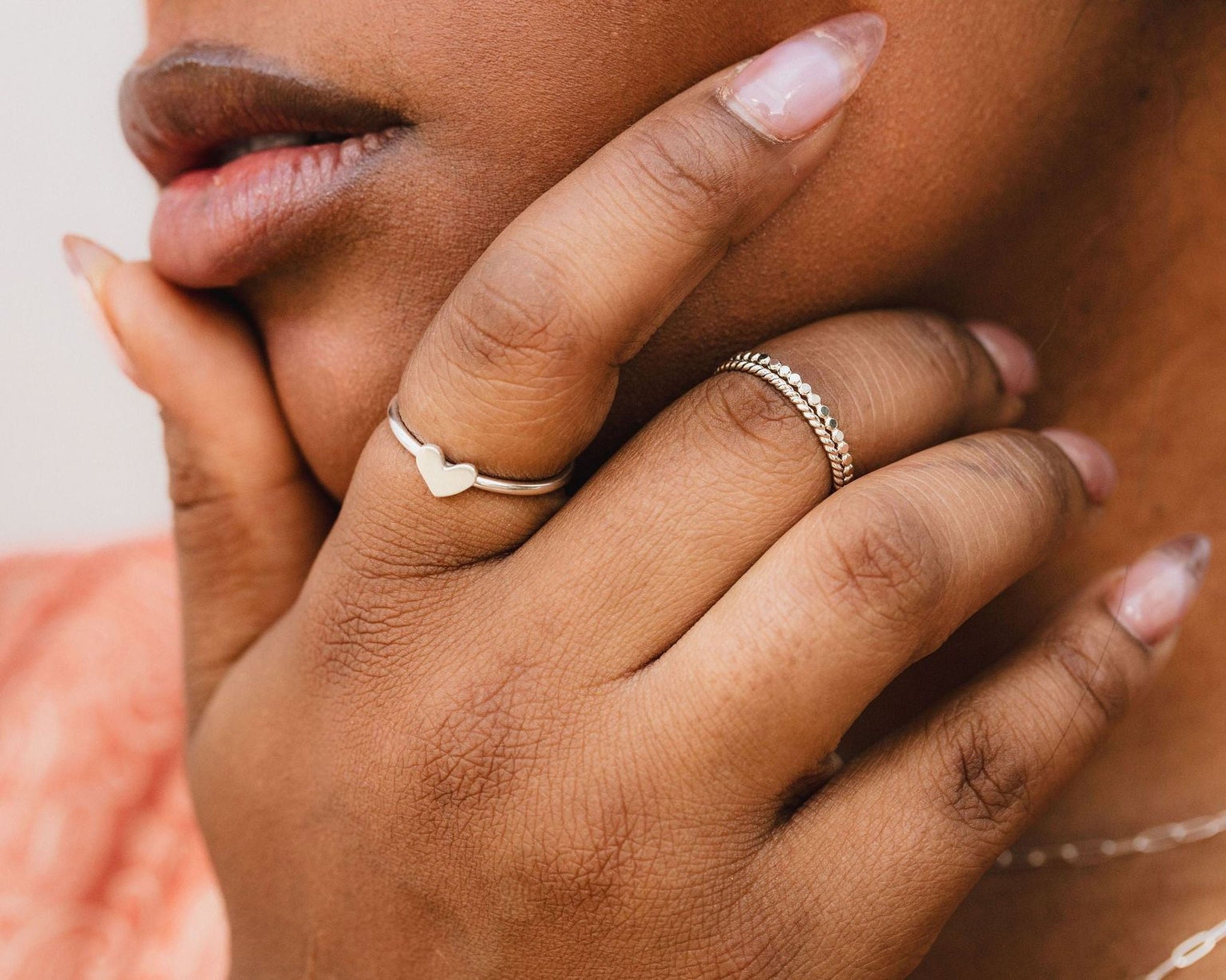 A close-up of a person's hand wearing two rings, one with a heart design and the other with a metallic band.
