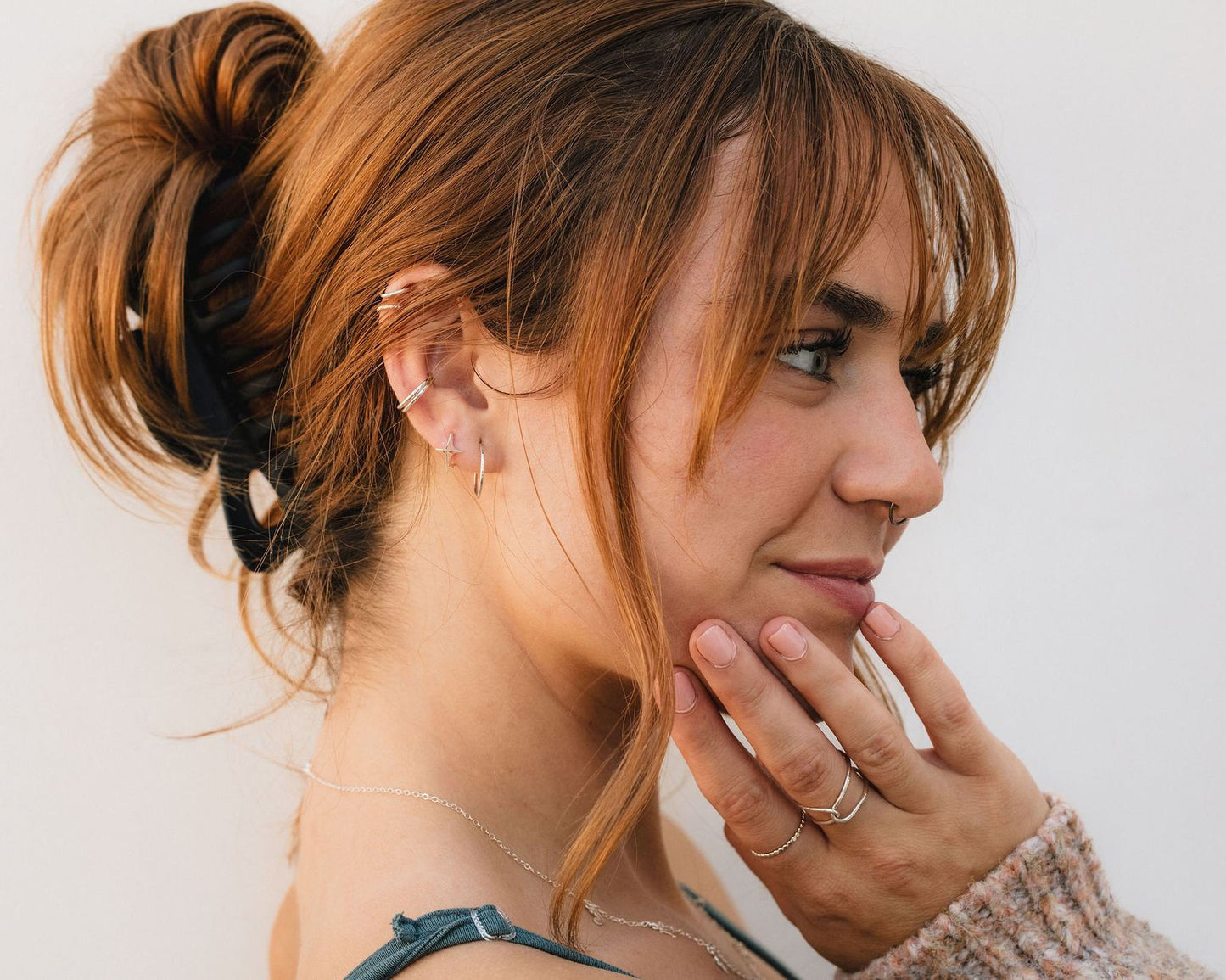 A woman with long, reddish-brown hair is shown in profile, her hand gently touching her face. She is wearing multiple rings on her fingers and has a casual, relaxed pose.
