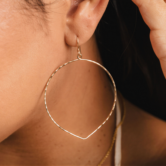 A close-up view of a person's ear wearing a gold hoop earring.