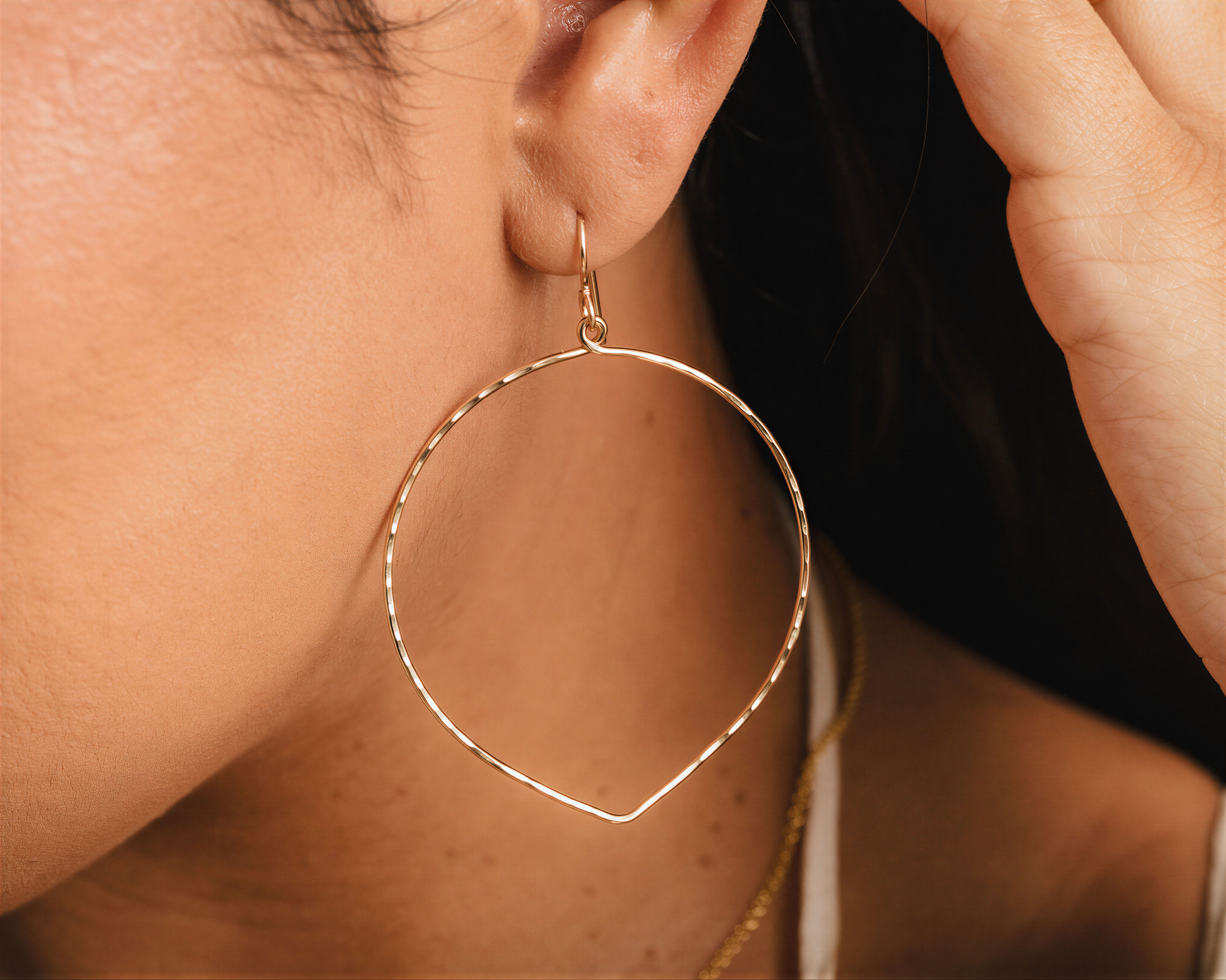 A close-up view of a person's ear wearing a gold hoop earring.