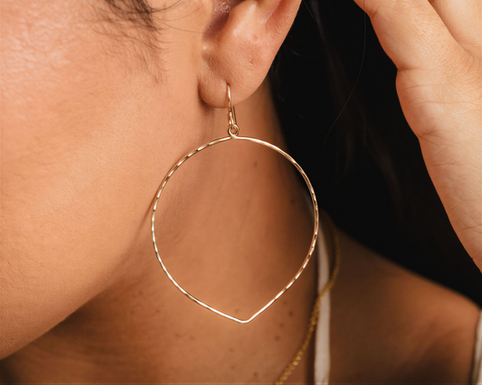 A close-up view of a person's ear wearing a gold hoop earring.