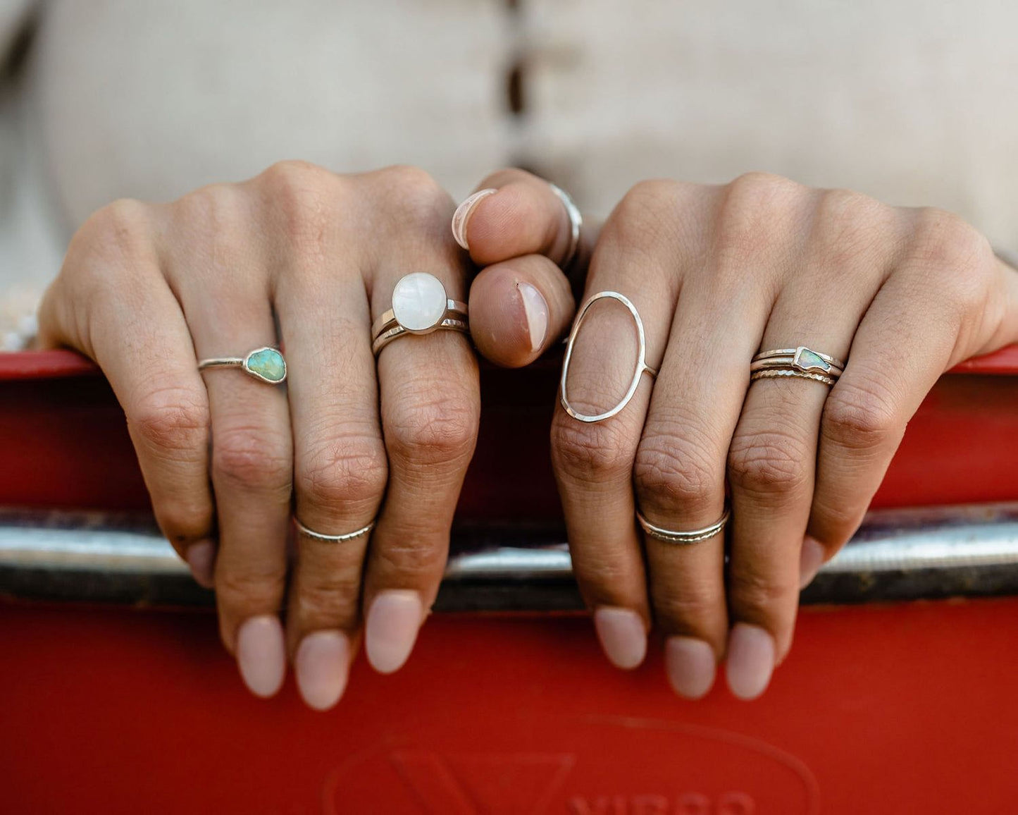 A close-up of a person's hands wearing multiple rings, including a ring with a large oval stone and other rings with various designs.
