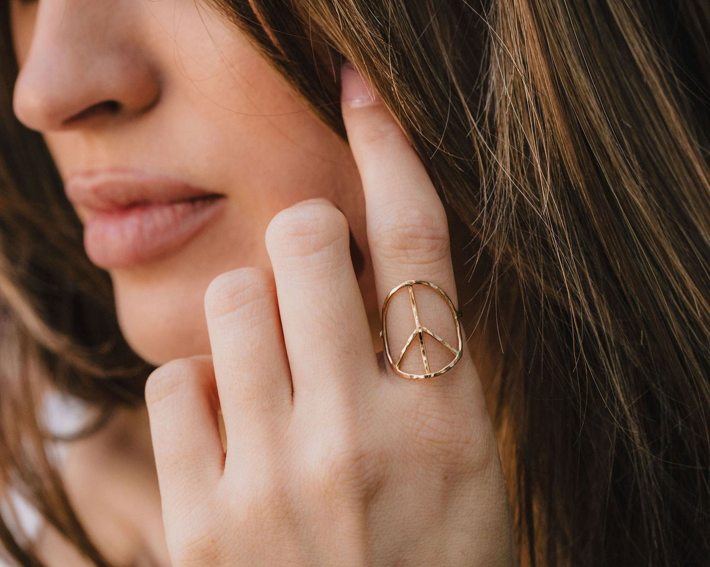 A close-up of a person's hand wearing a peace sign ring, with their hair visible in the background.
