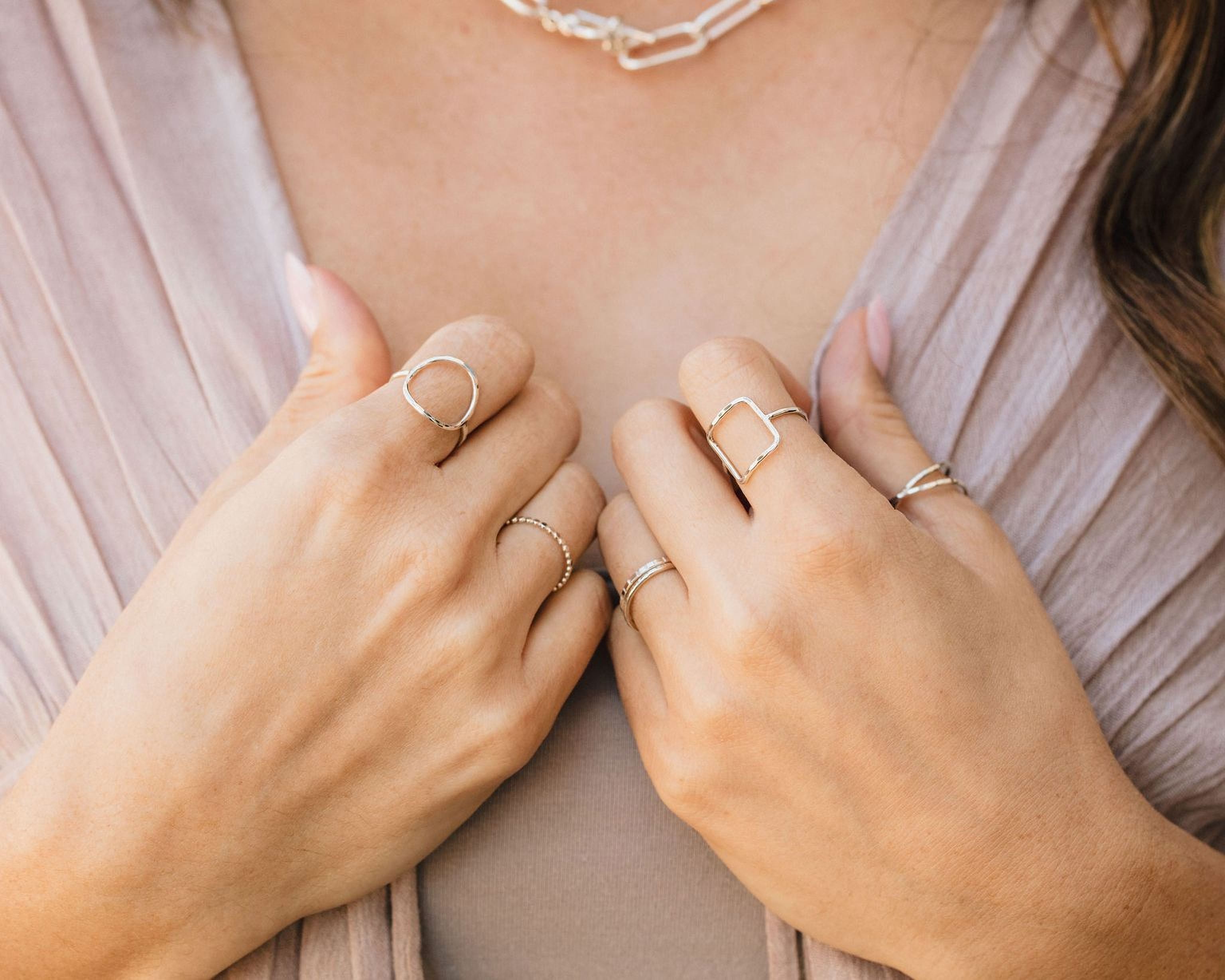 A close-up view of a person's hands wearing multiple rings on their fingers.