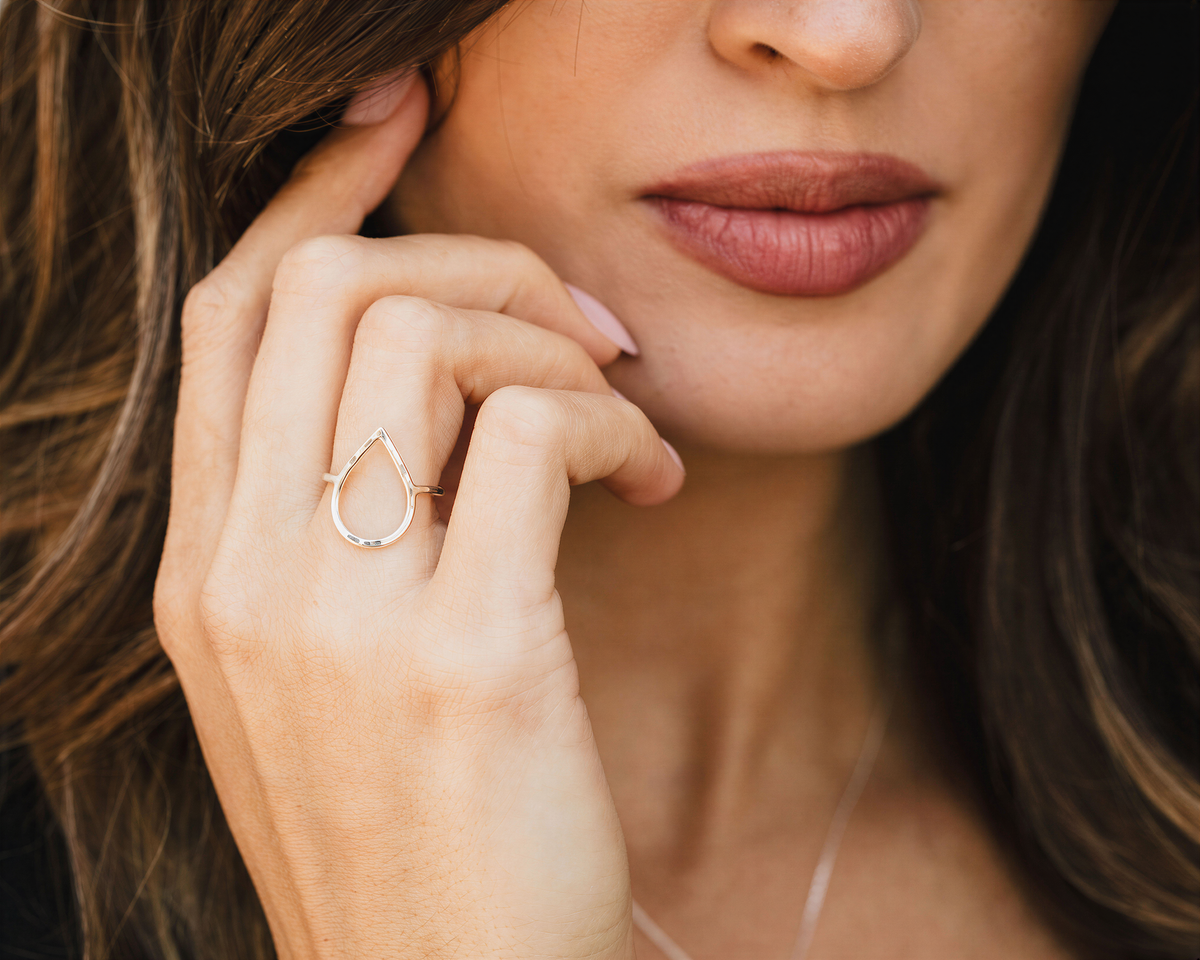 A close-up of a woman's hand wearing a ring, with her lips and chin visible.