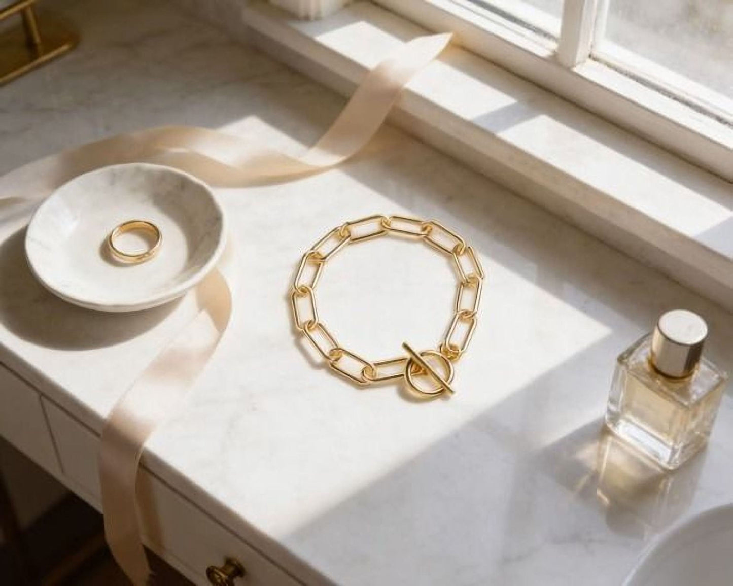 a white marble countertop with various accessories, including a ring, a bracelet, and a bottle of perfume.