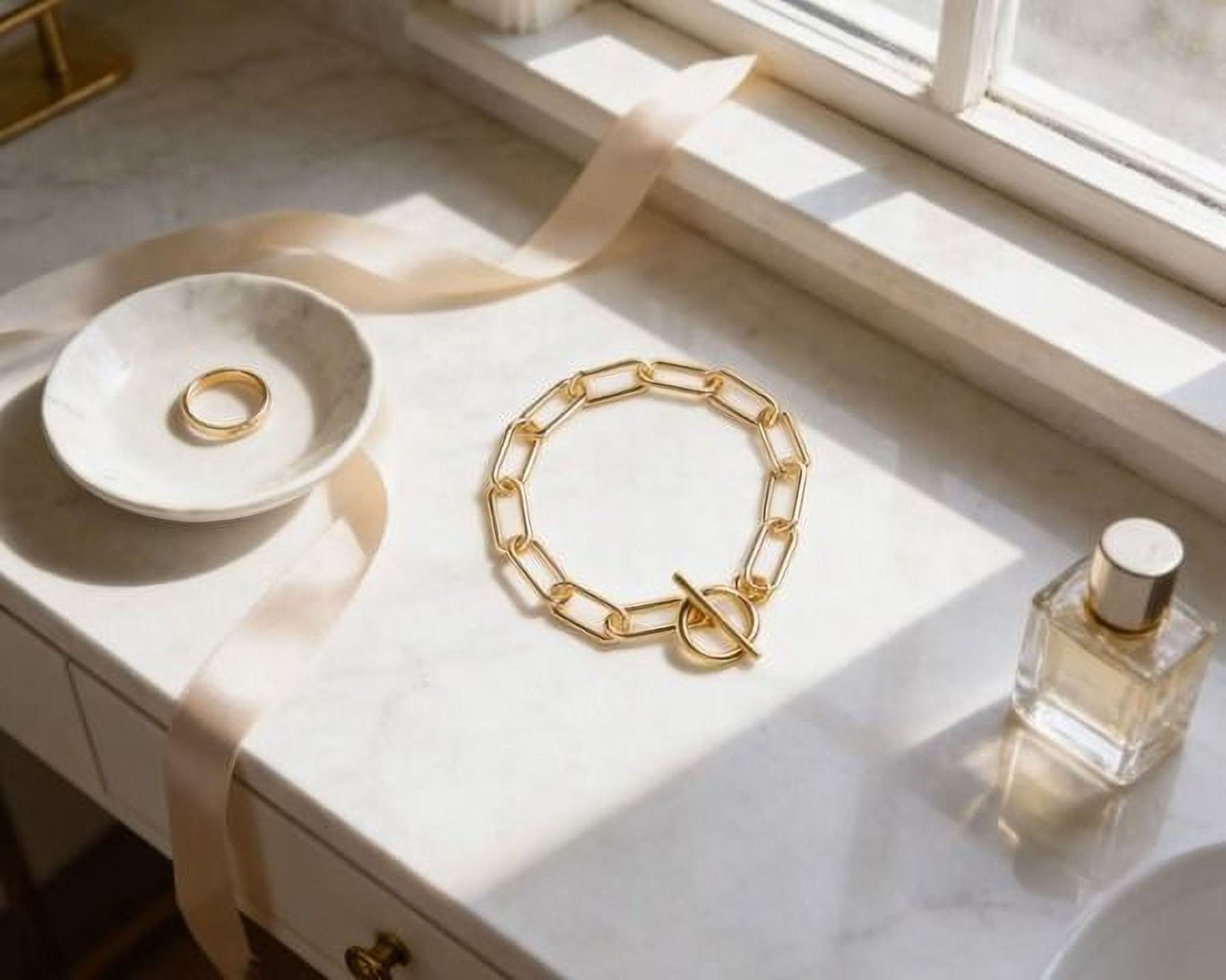 a white marble countertop with various accessories, including a ring, a bracelet, and a bottle of perfume.