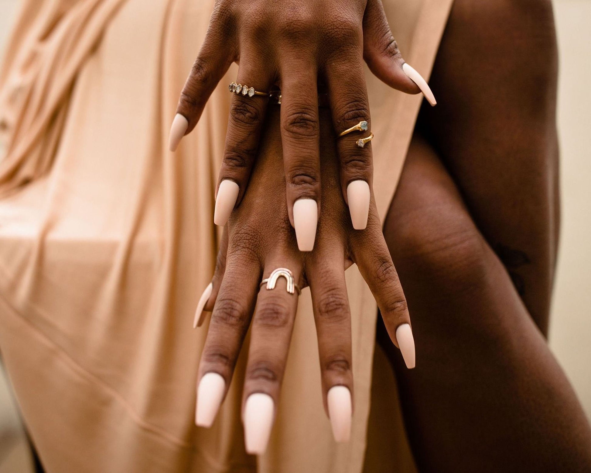A close-up of a person's hands with long, painted fingernails and multiple rings on their fingers.