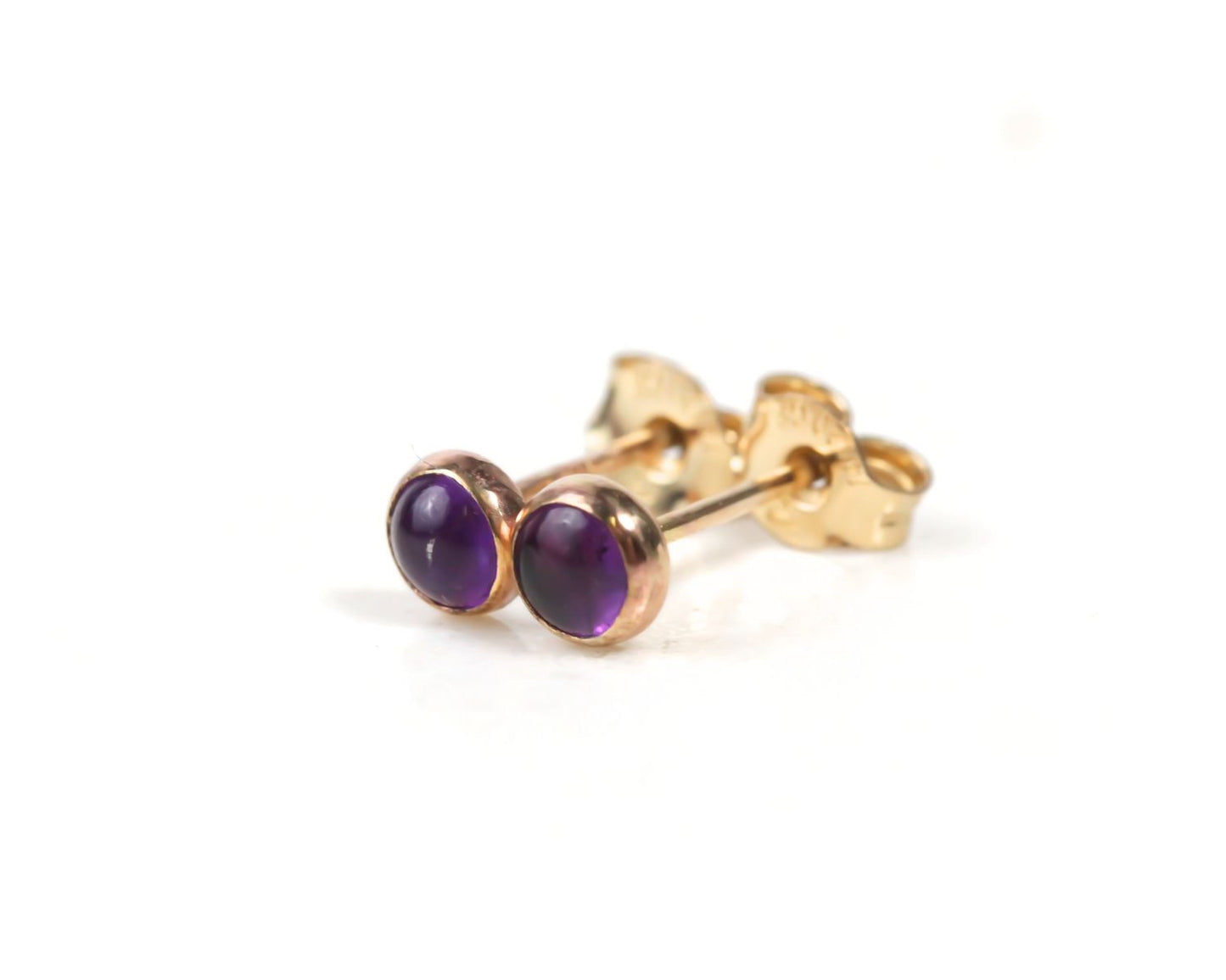 A pair of gold earrings with purple gemstones, specifically amethyst, are shown against a white background.