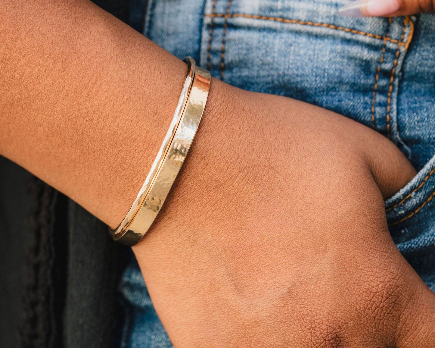 A gold bracelet is worn on a person's wrist, with their hand partially visible in the background.