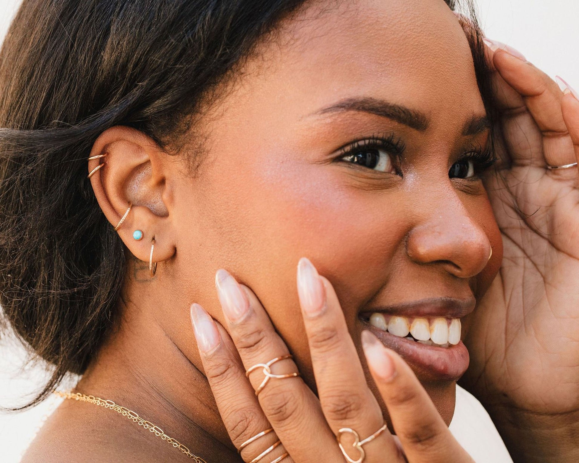 A close-up portrait of a smiling woman with dark hair and multiple rings on her fingers.