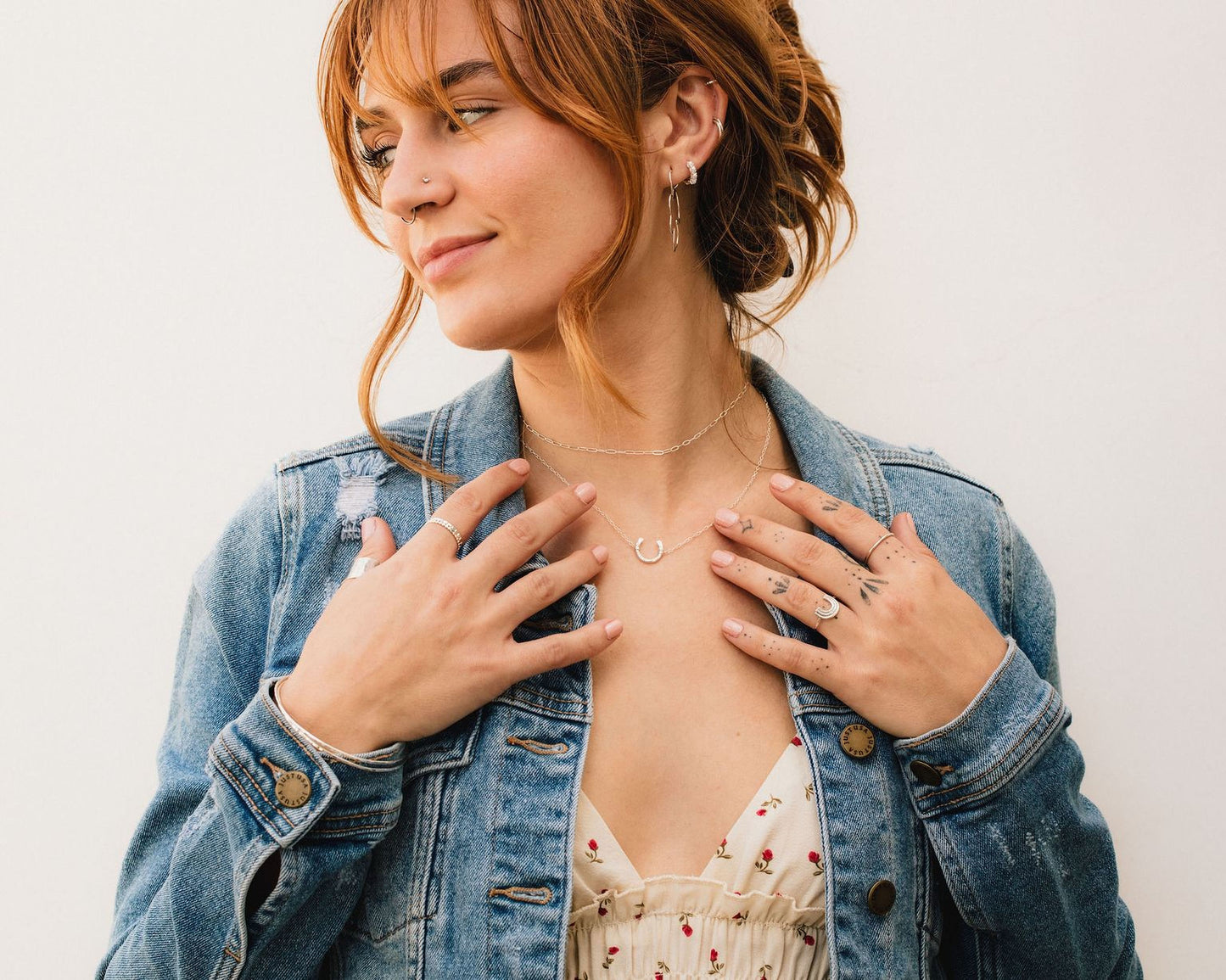 A woman with red hair wearing a denim jacket and a floral top, smiling and looking to her left.