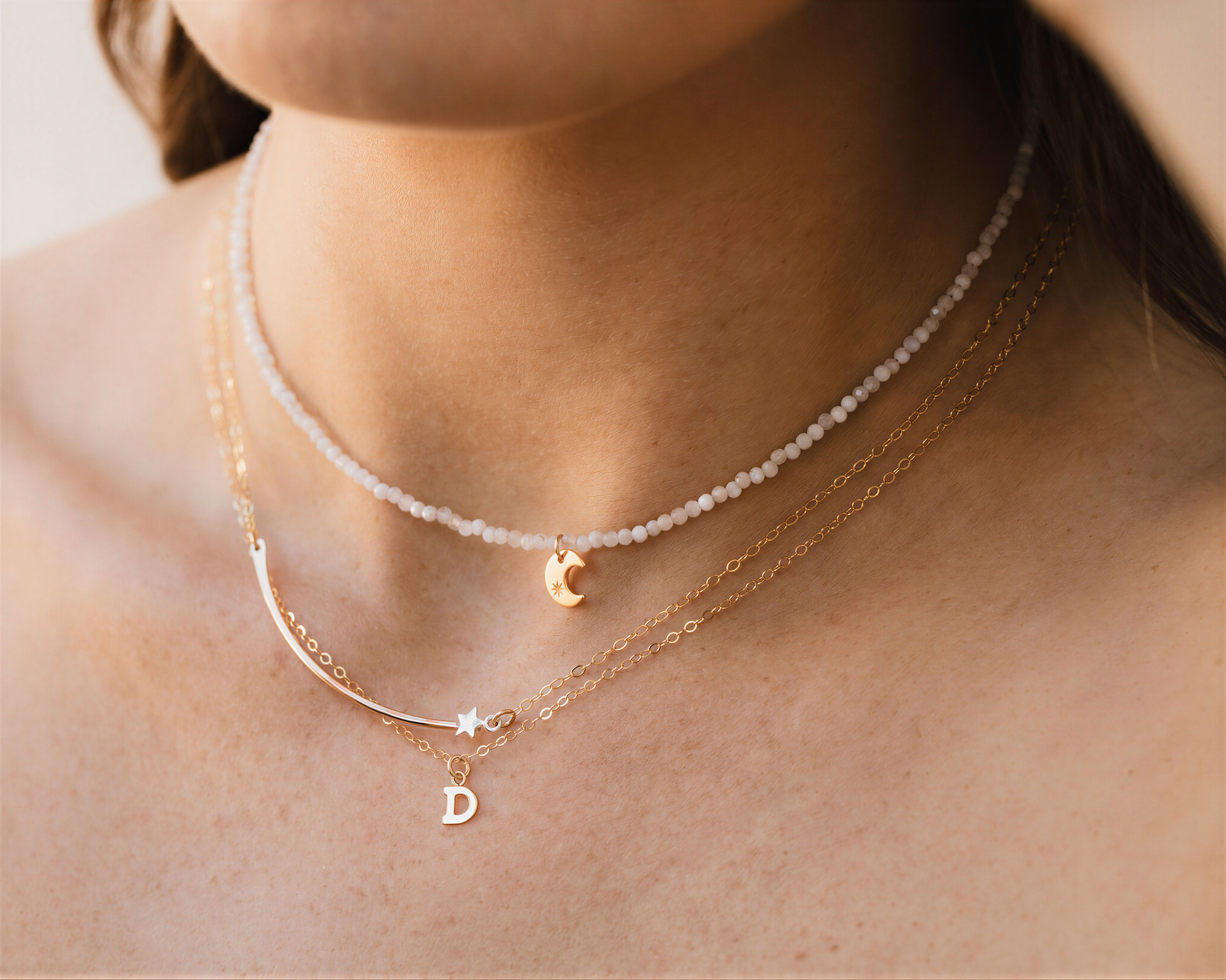 A close-up view of a person's neck adorned with multiple necklaces, including a beaded necklace, a charm necklace, and a pendant necklace.
