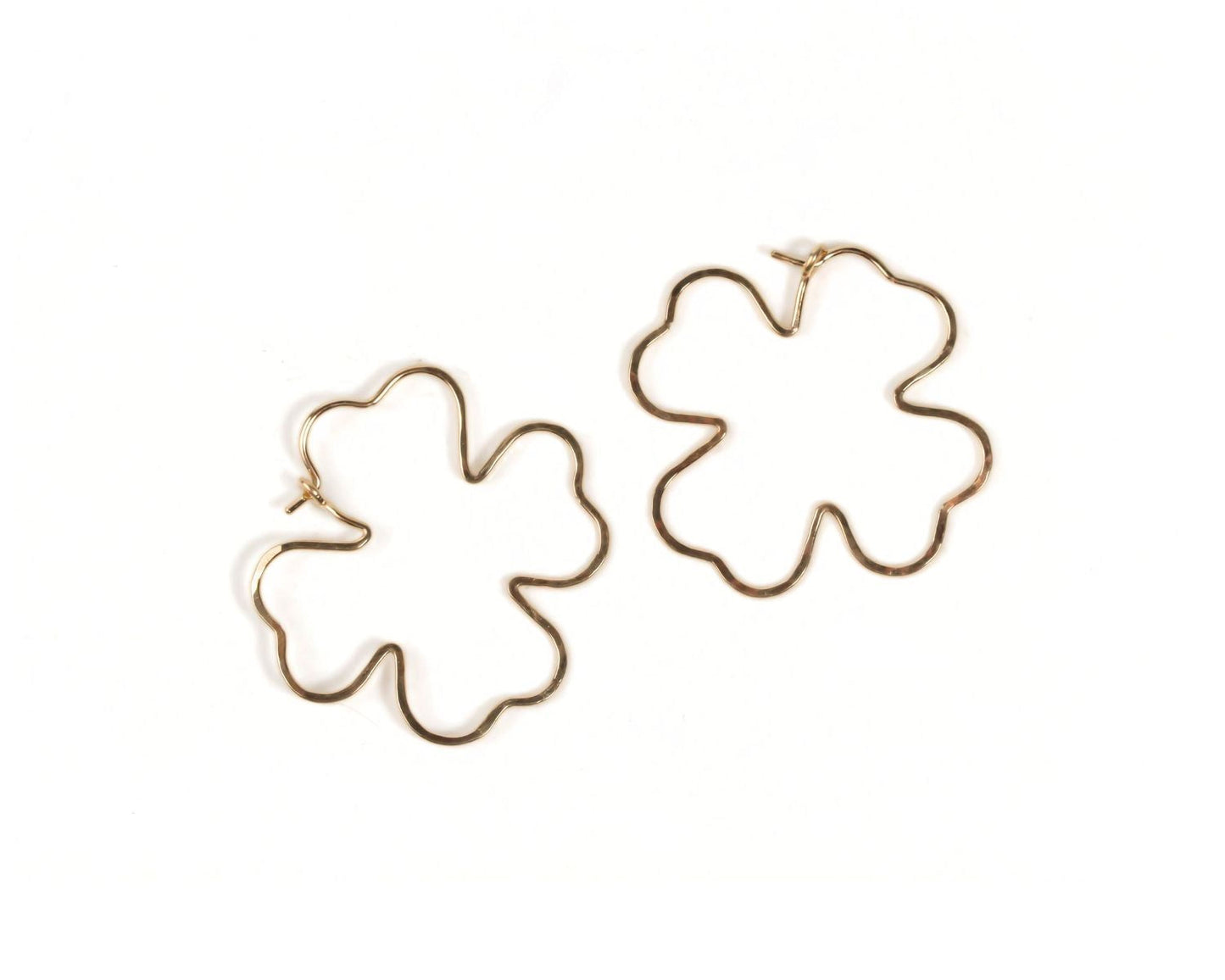two gold-colored earrings in the shape of leaves, specifically clovers.