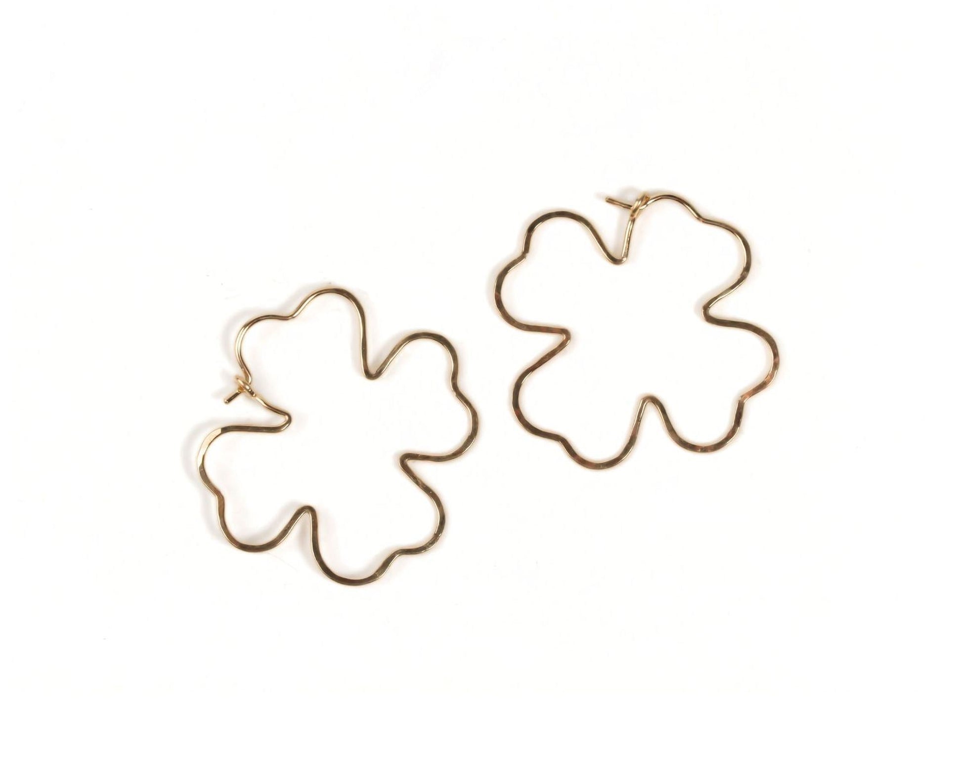two gold-colored earrings in the shape of leaves, specifically clovers.