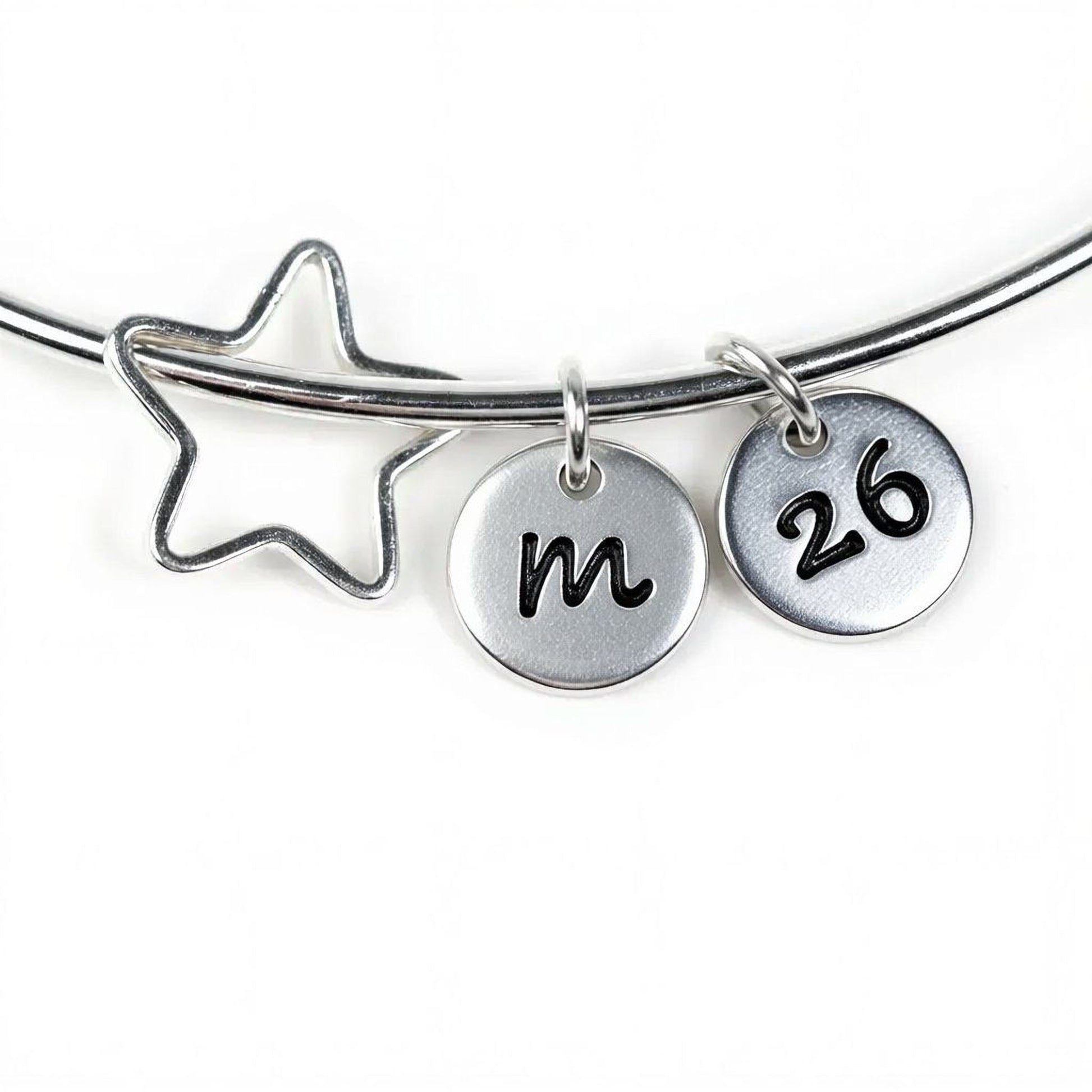 A silver bracelet with a star-shaped charm and two metal charms attached to it, each with a number on it.
