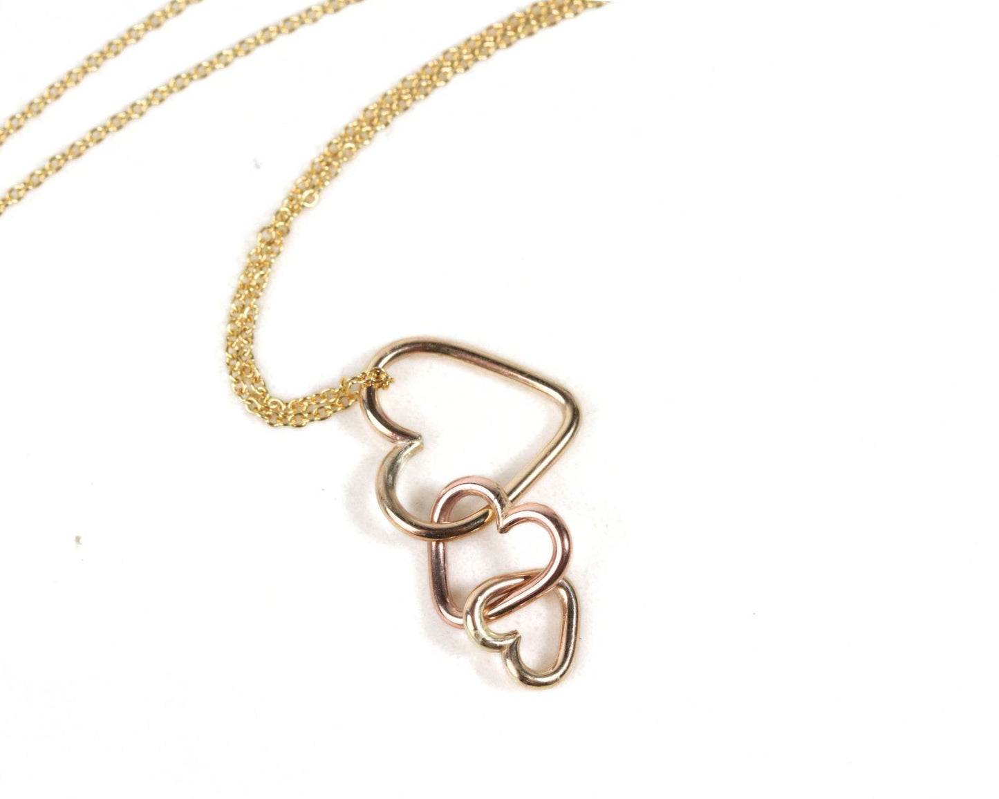 A gold necklace with a pendant in the shape of a heart, connected to other heart-shaped pendants.