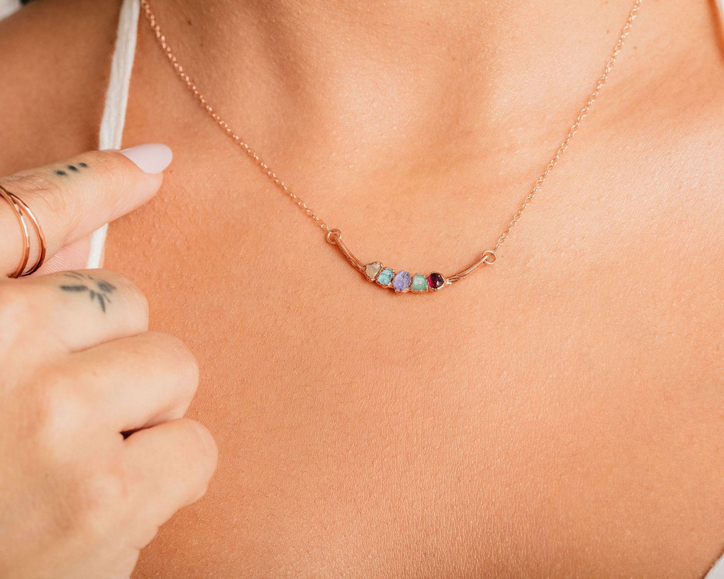 A close-up of a person's hand wearing a necklace with a colorful pendant.