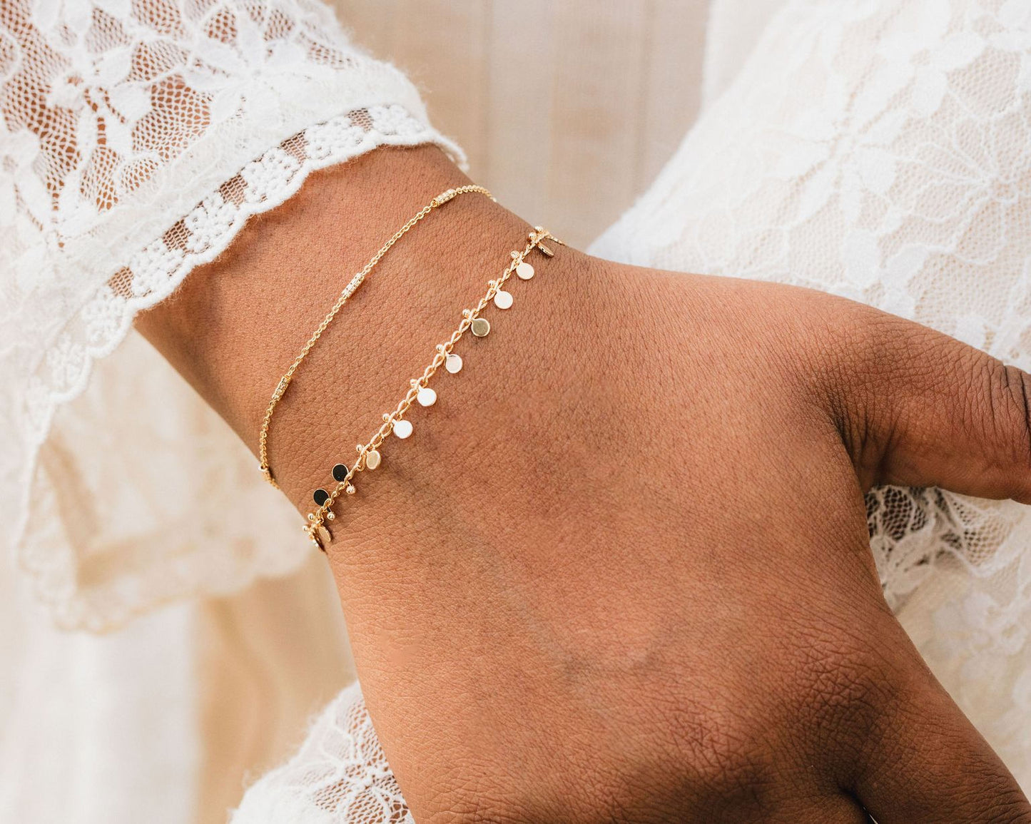 A close-up view of a person's wrist wearing two gold-colored bracelets with small dangling charms.