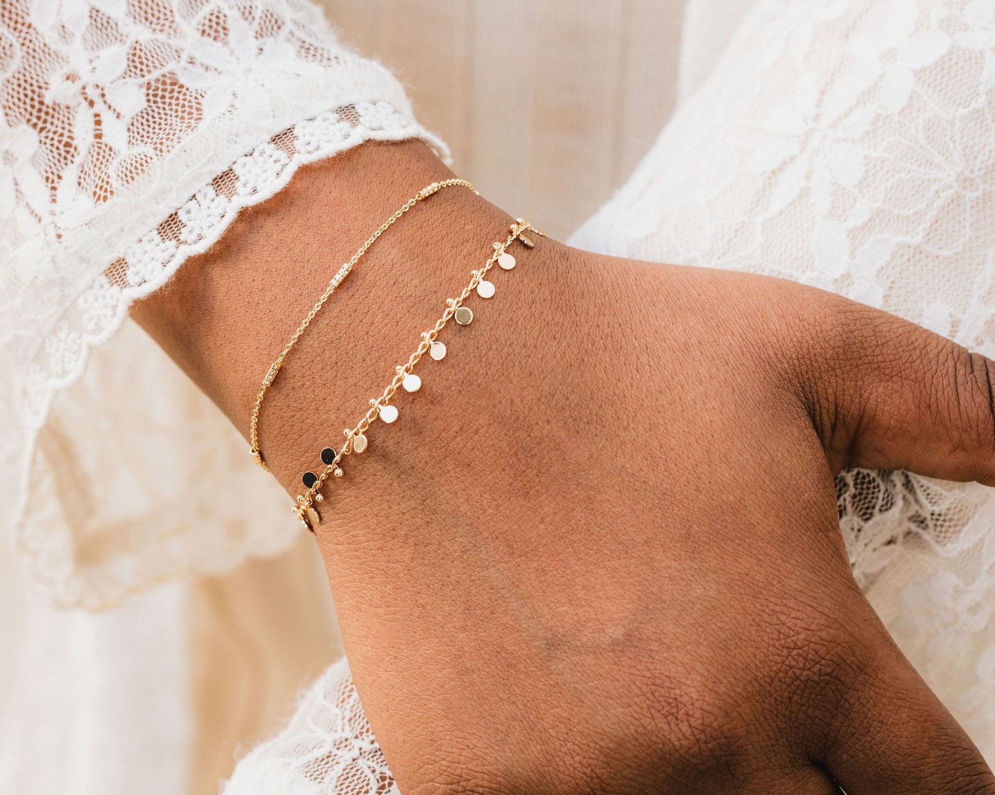 A close-up view of a person's wrist wearing two gold-colored bracelets with small dangling charms.