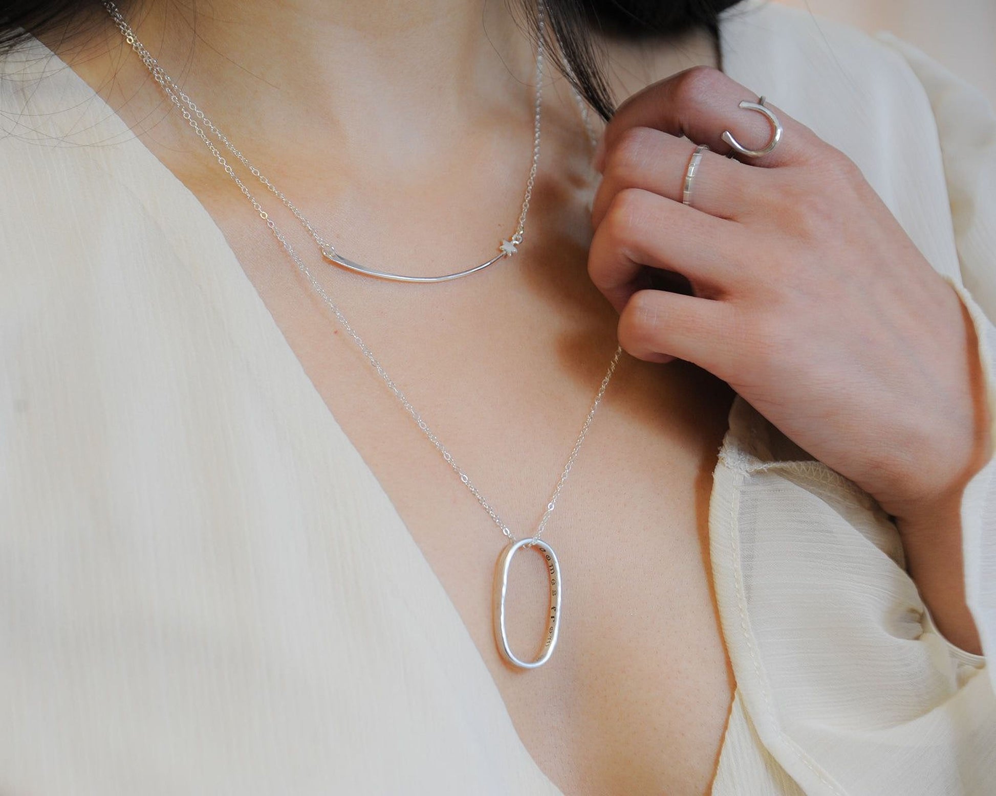 A close-up view of a person's neck and chest area, wearing a necklace with a pendant and a ring on their finger.