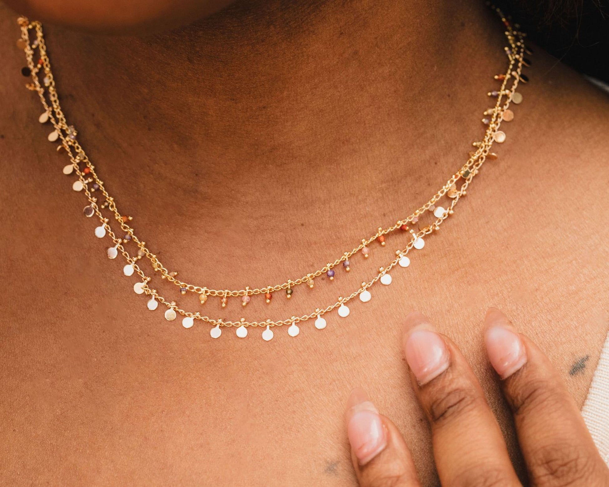 A close-up view of a gold necklace with small circular charms on a person's neck.
