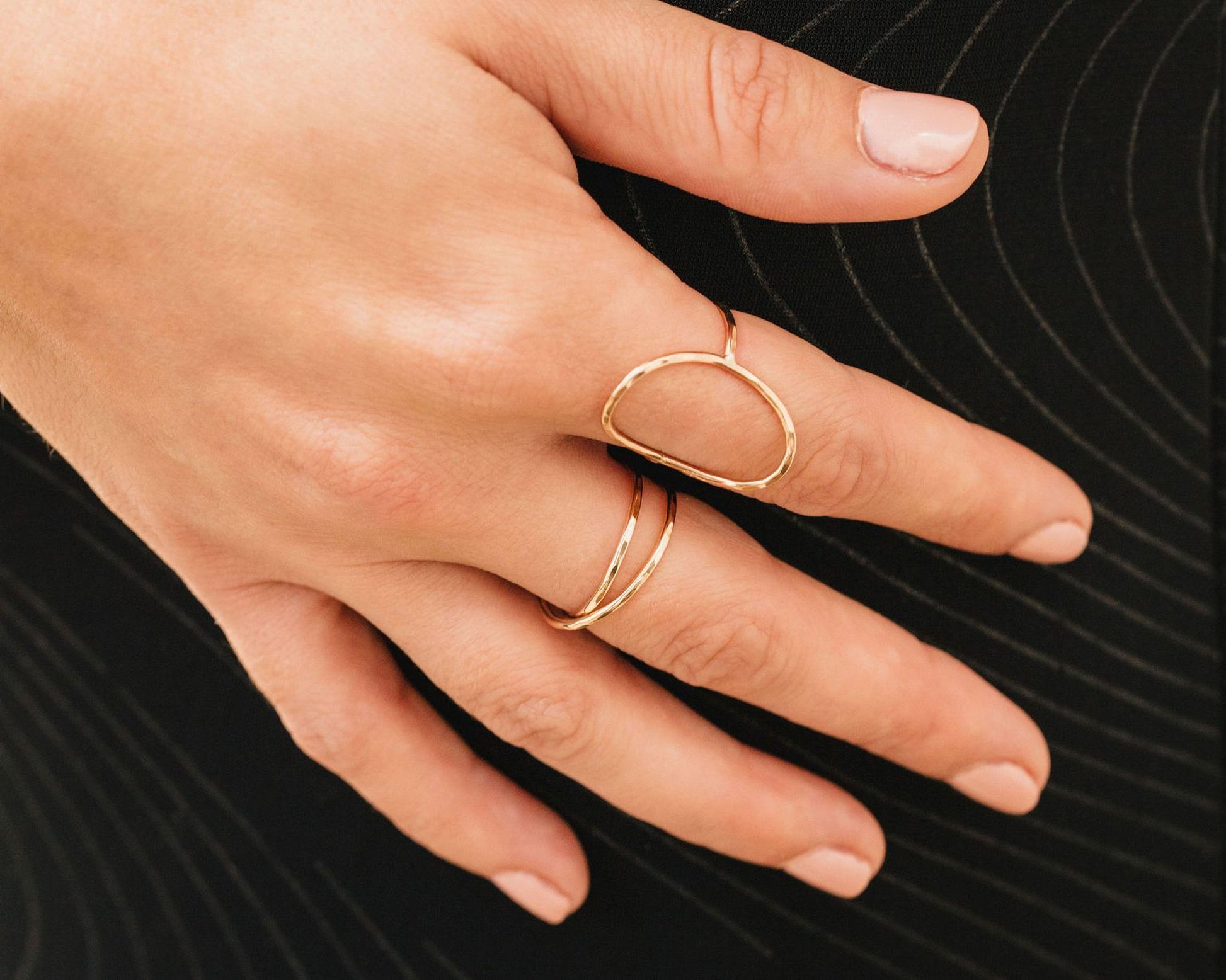 A close-up view of a person's hand wearing two gold rings on the fingers.
