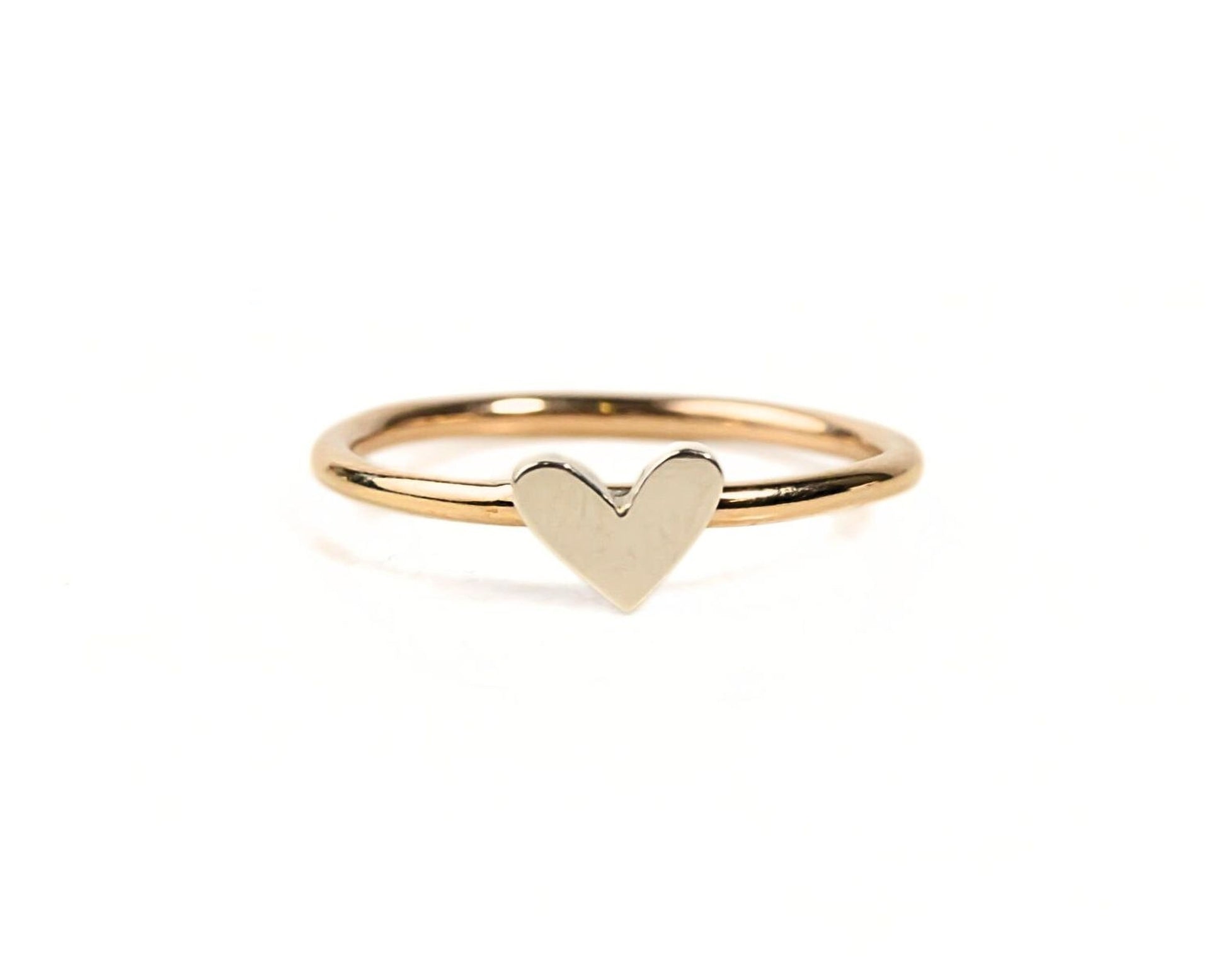 A simple gold ring with a heart-shaped charm in the center.