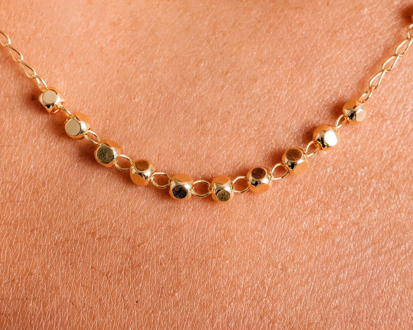 A close-up view of a gold necklace with small, round beads on a person's skin.