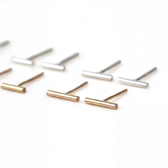 A collection of small, thin metal earrings in various colors, including gold, silver, and bronze, arranged on a white background.