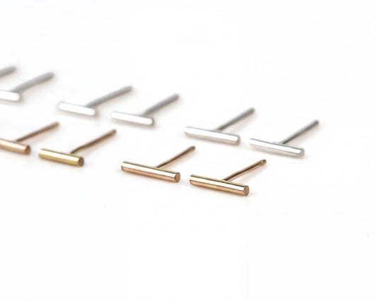 A collection of small, thin metal earrings in various colors, including gold, silver, and bronze, arranged on a white background.