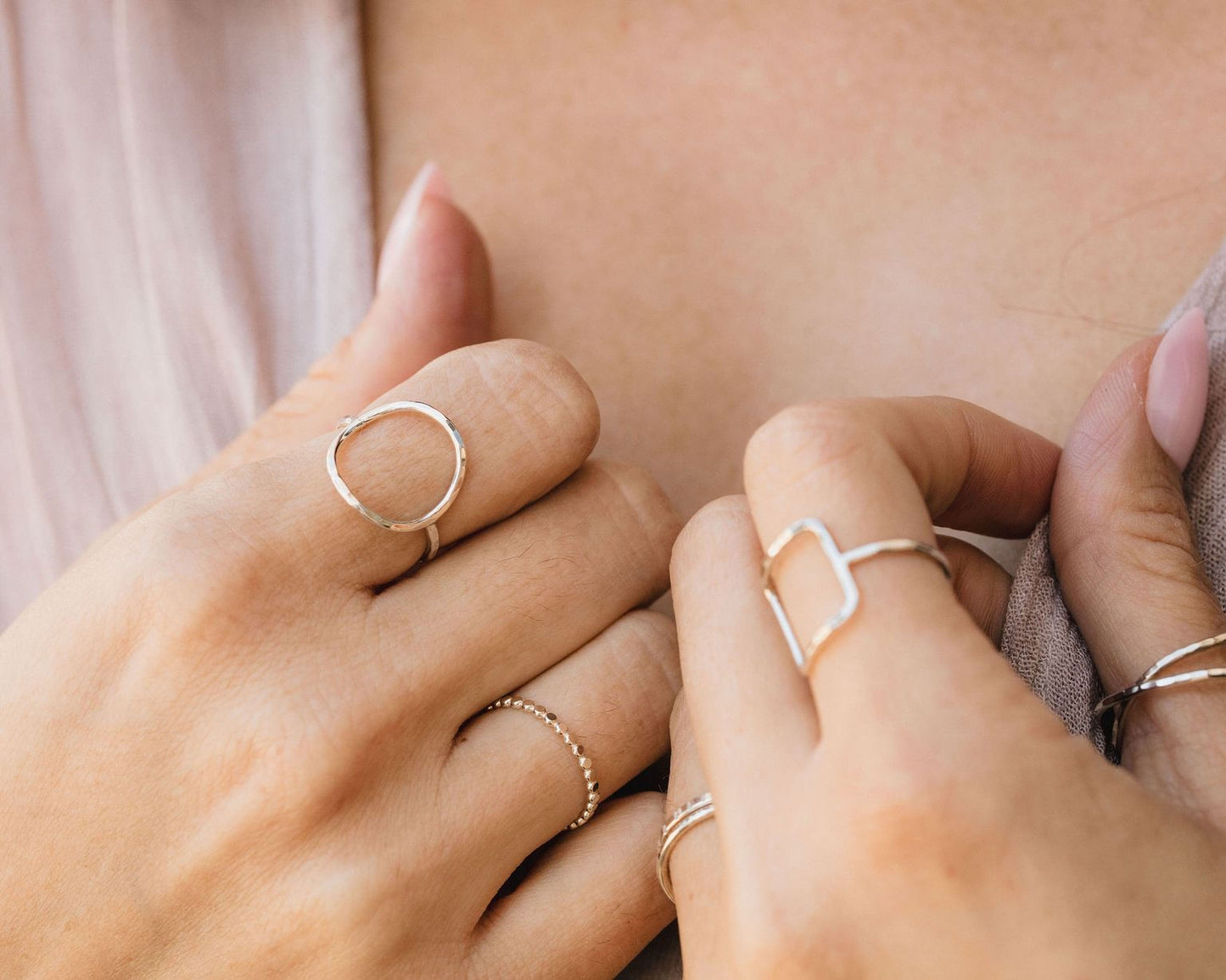 A close-up view of a person's hands wearing multiple rings, including a ring with a circular design and another with a rectangular shape.