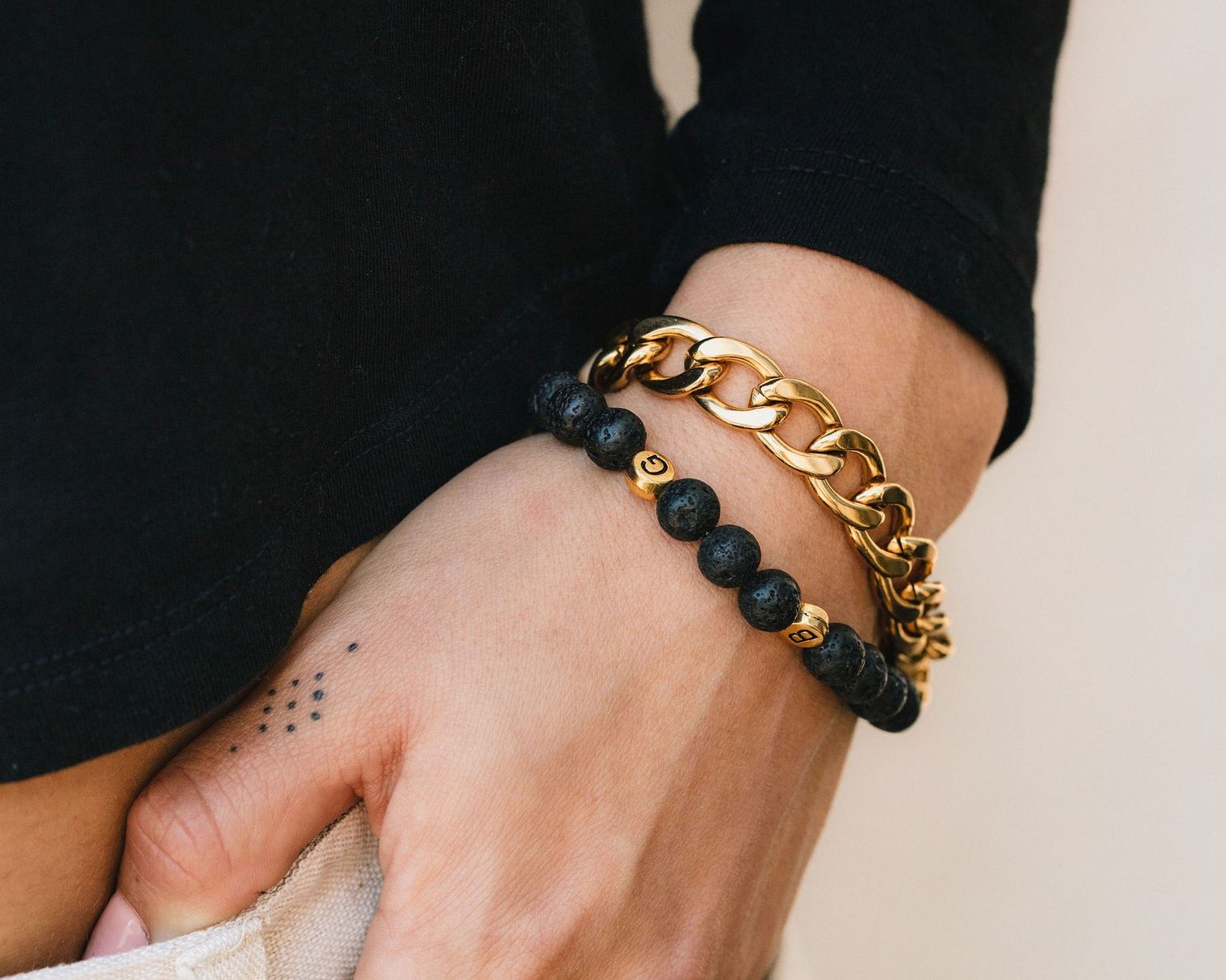 A close-up of a person's hand wearing two bracelets, one made of beads and the other a chain bracelet.