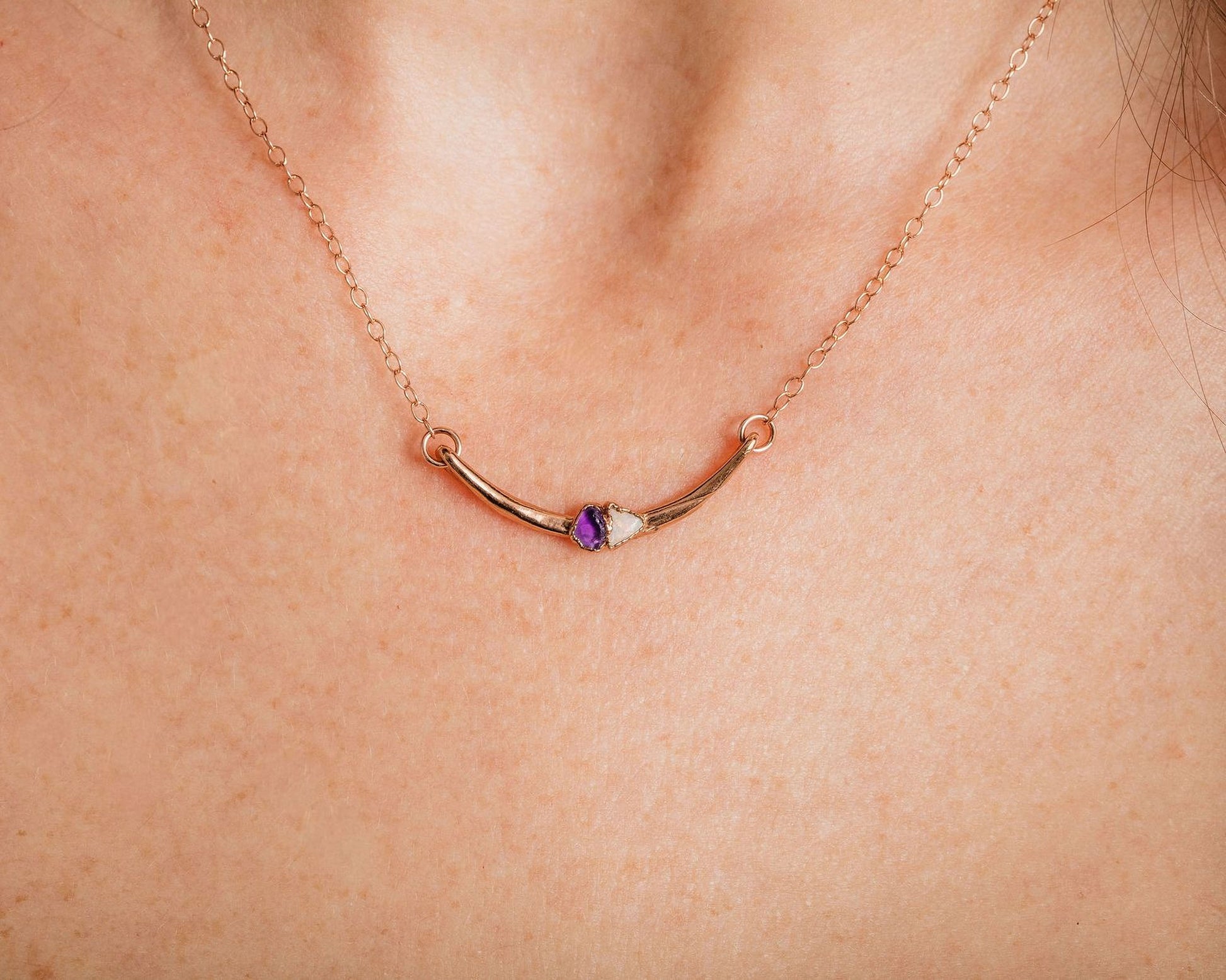 A close-up view of a gold necklace with a curved pendant featuring a purple gemstone.