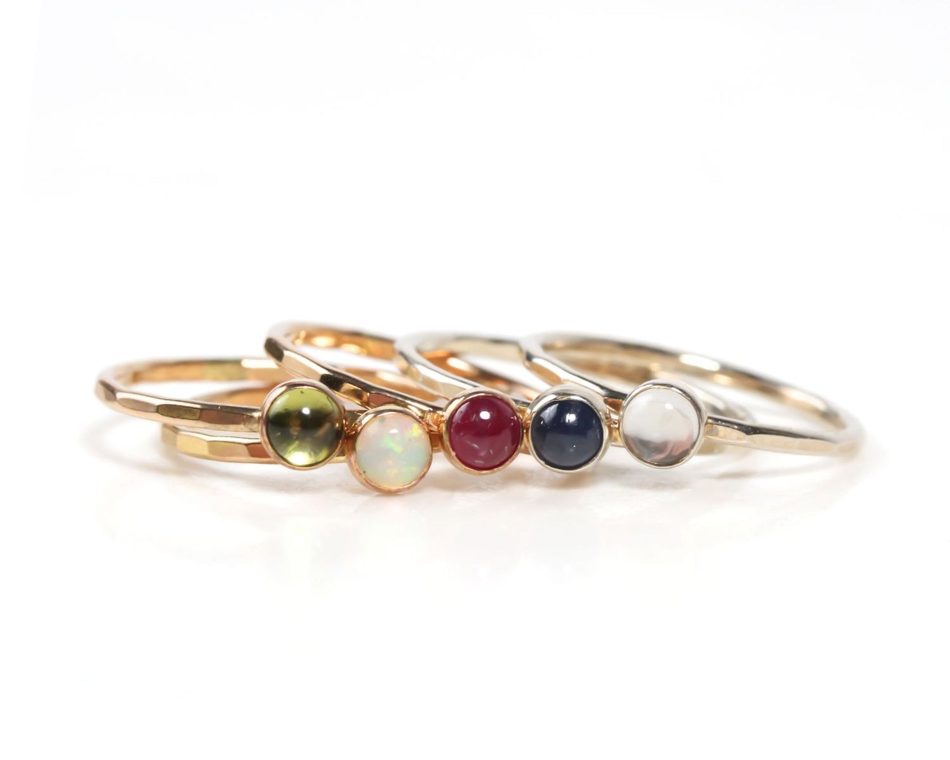 A collection of gold rings with colorful gemstones, including opals, garnets, and diamonds, arranged in a row.