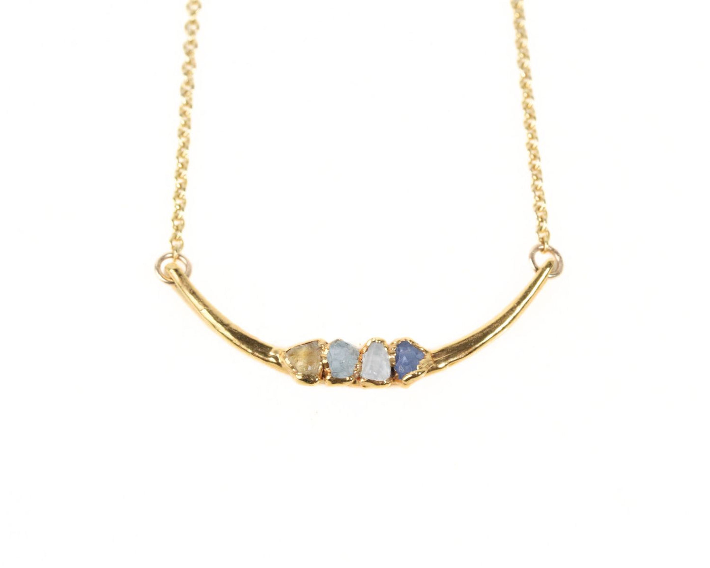 A gold necklace with a curved pendant featuring three gemstones.
