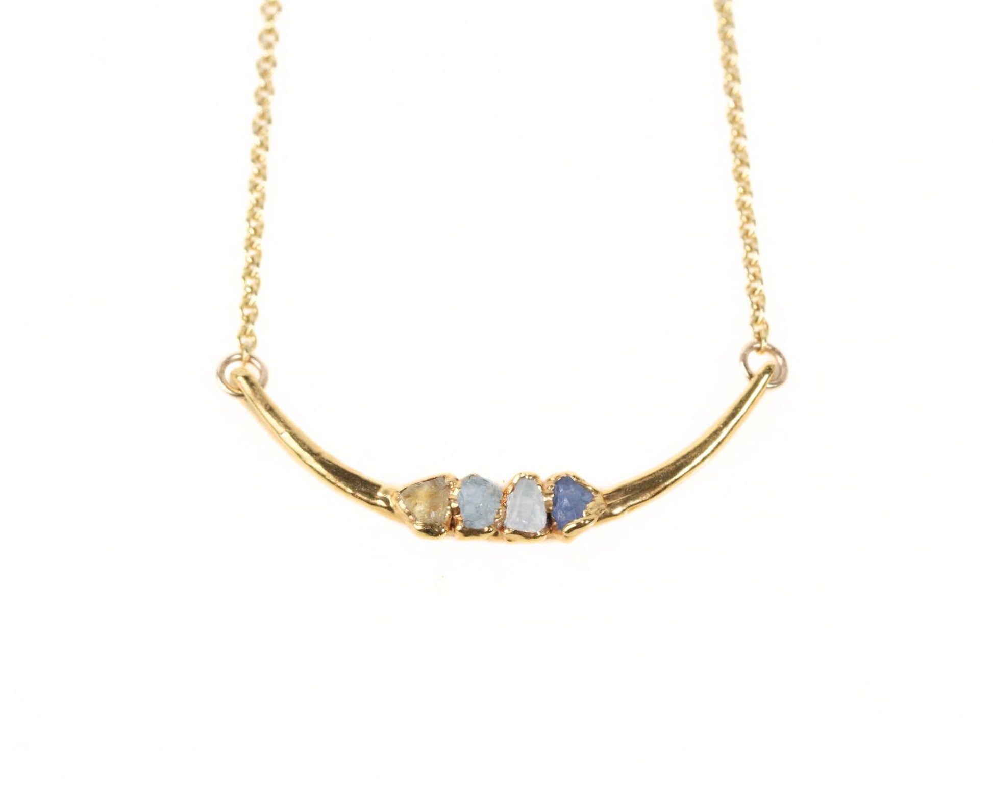 A gold necklace with a curved pendant featuring three gemstones.