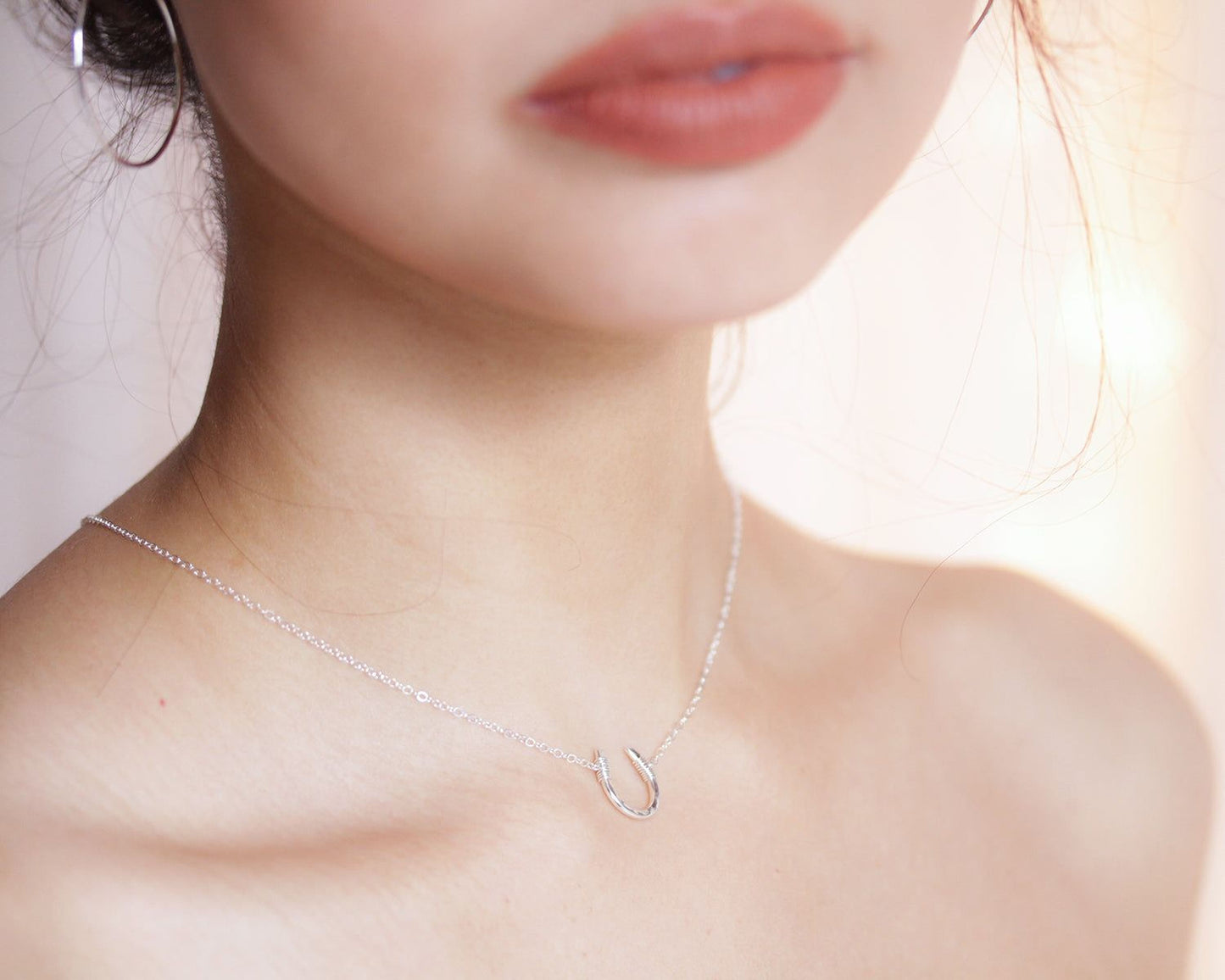 A close-up of a woman's neck and chest area, with a delicate silver necklace featuring a small pendant.