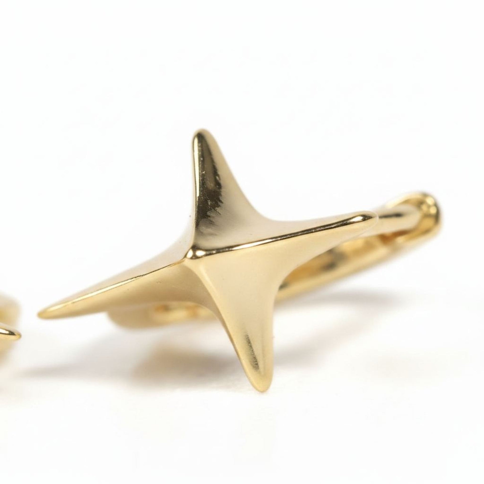 A close-up image of a shiny gold earring with a pointed, star-like shape.