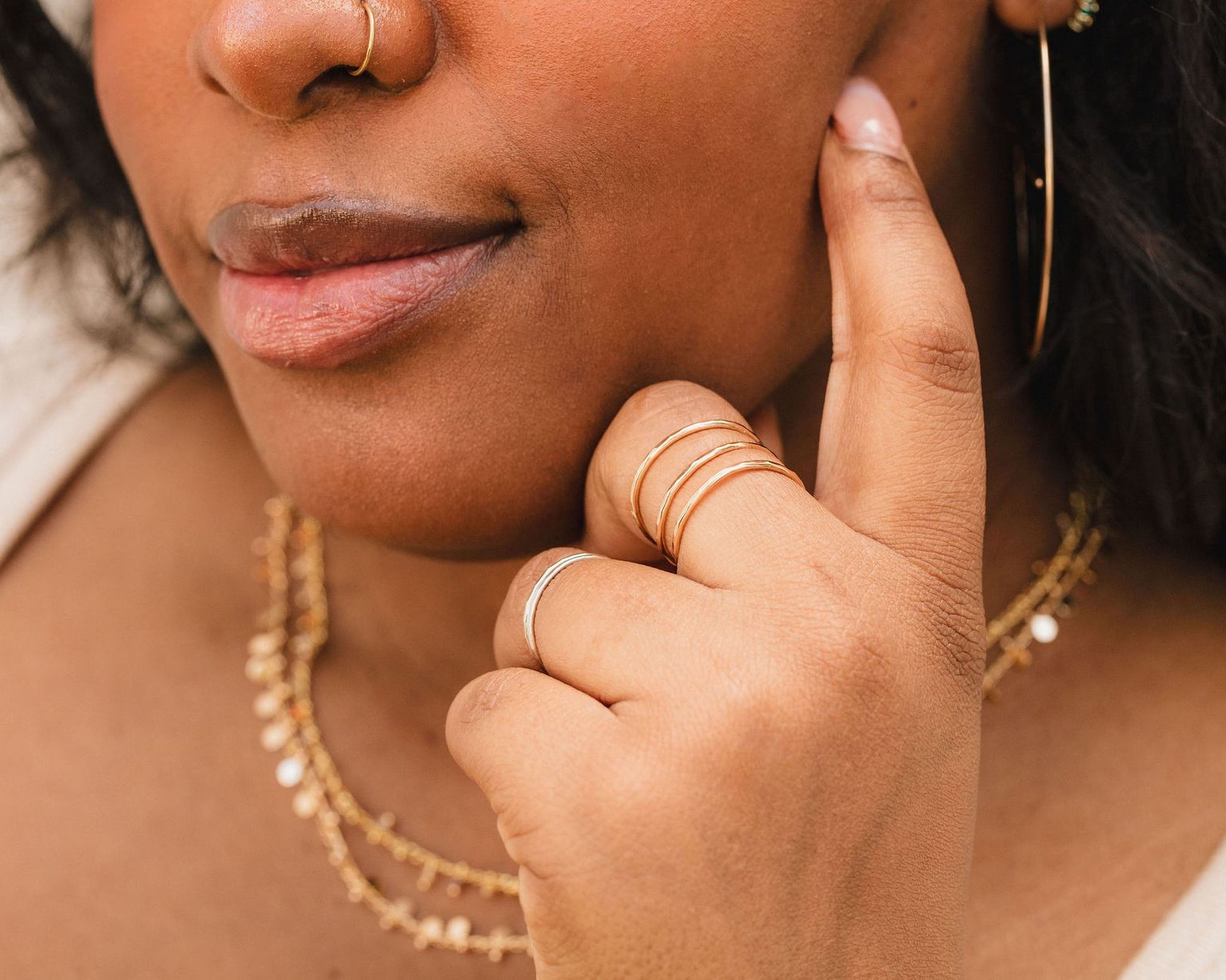 A close-up of a person's face, focusing on their hand and fingers adorned with multiple rings.