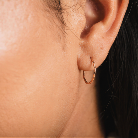 A close-up view of a person's ear with a gold hoop earring.