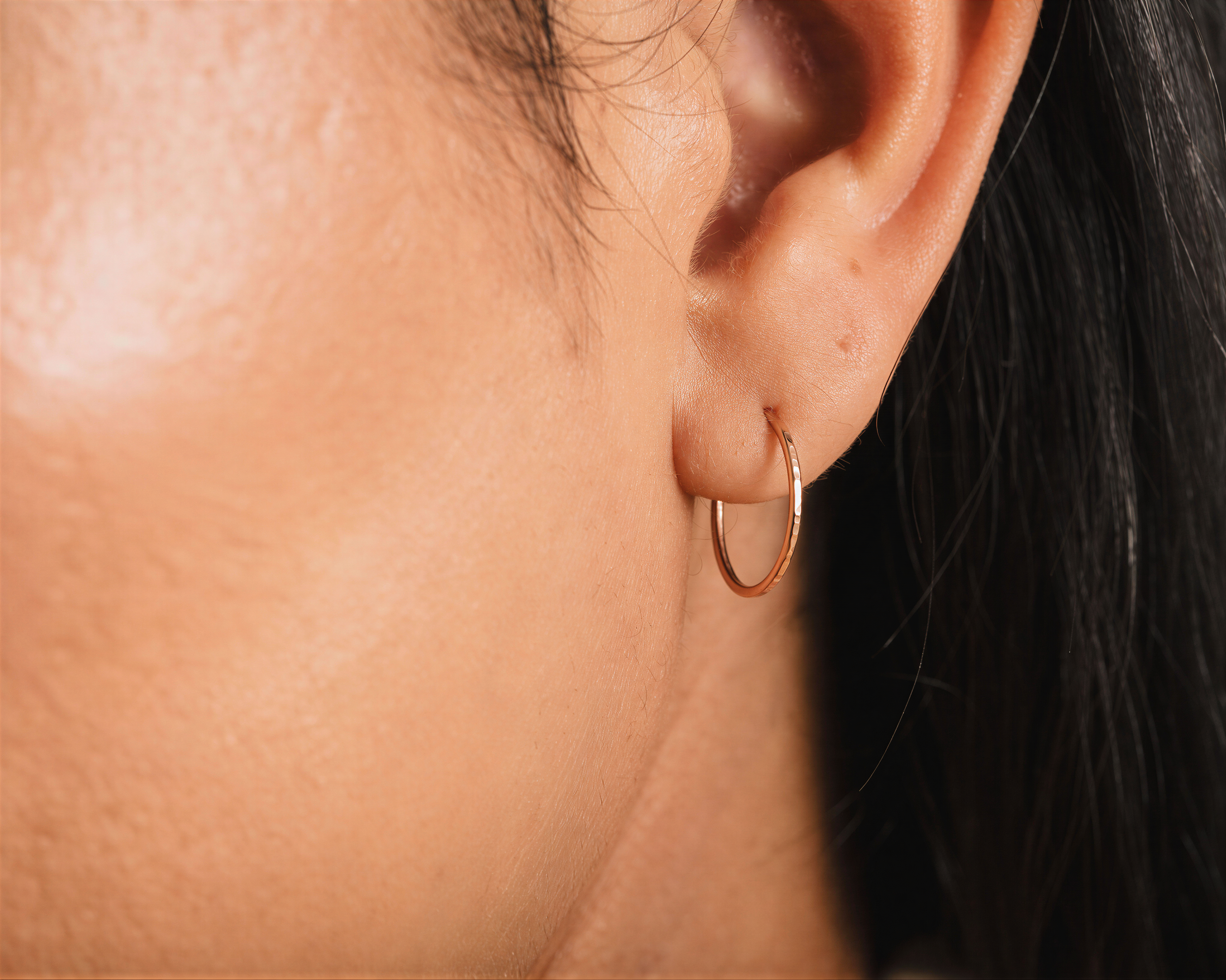 A close-up view of a person's ear with a gold hoop earring.