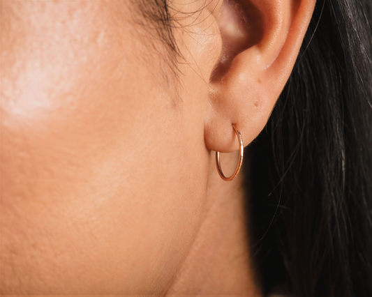 A close-up view of a person's ear with a gold hoop earring.