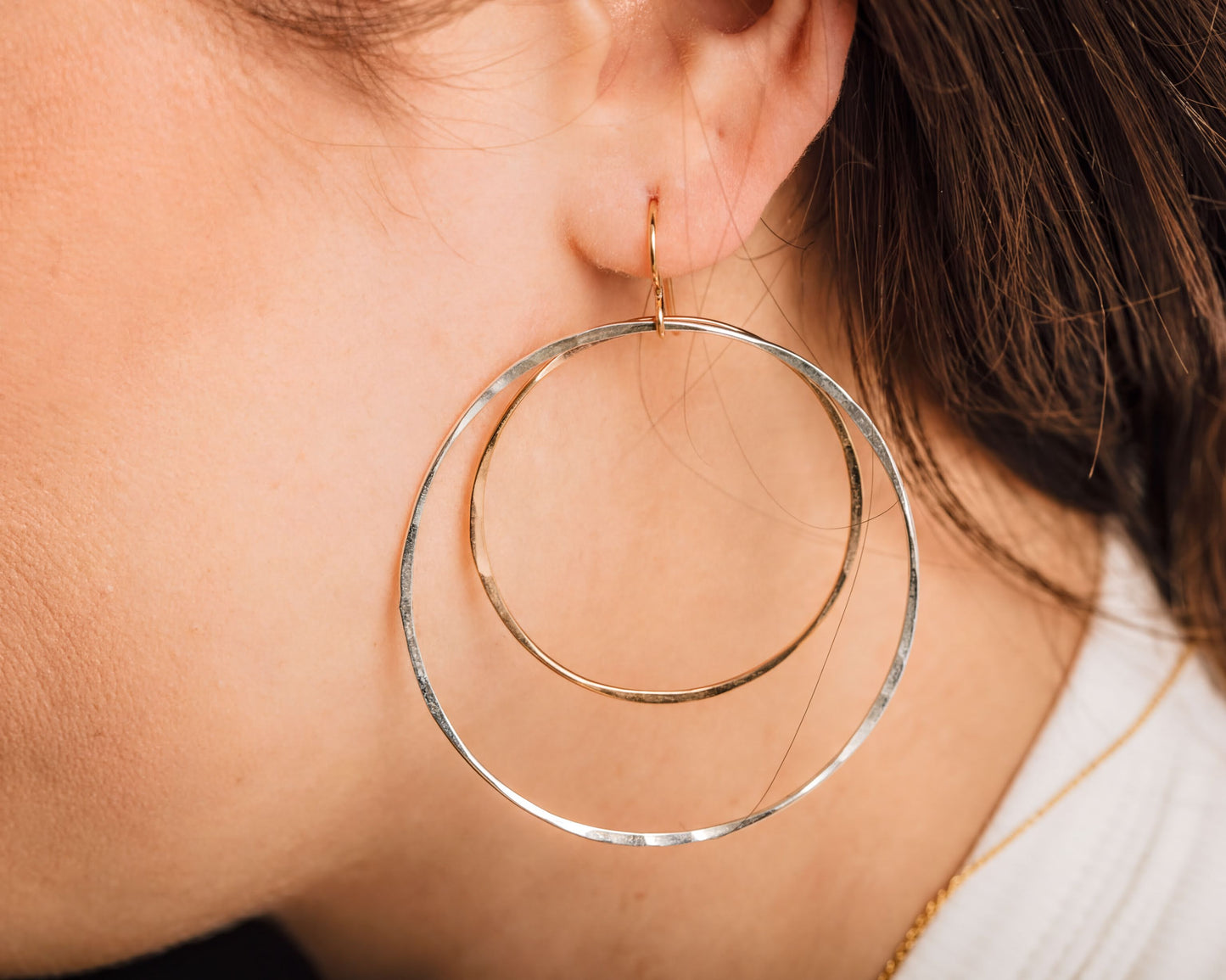 A close-up of a person's ear wearing large, gold-toned hoop earrings.