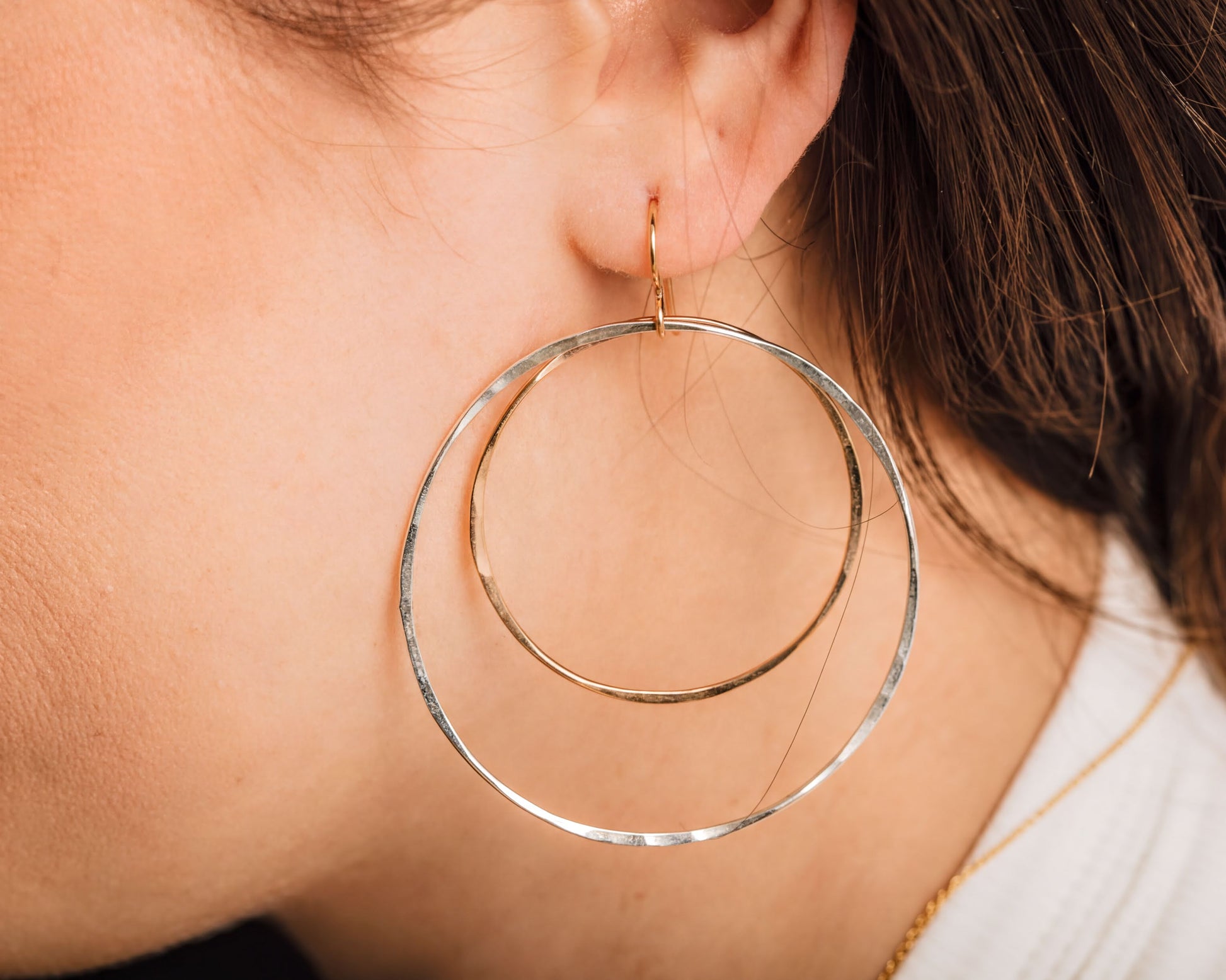 A close-up of a person's ear wearing large, gold-toned hoop earrings.