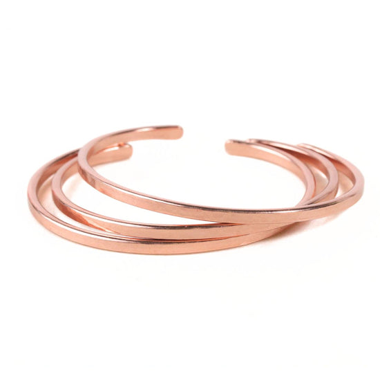 A group of copper-colored bracelets arranged in a circular pattern against a white background.